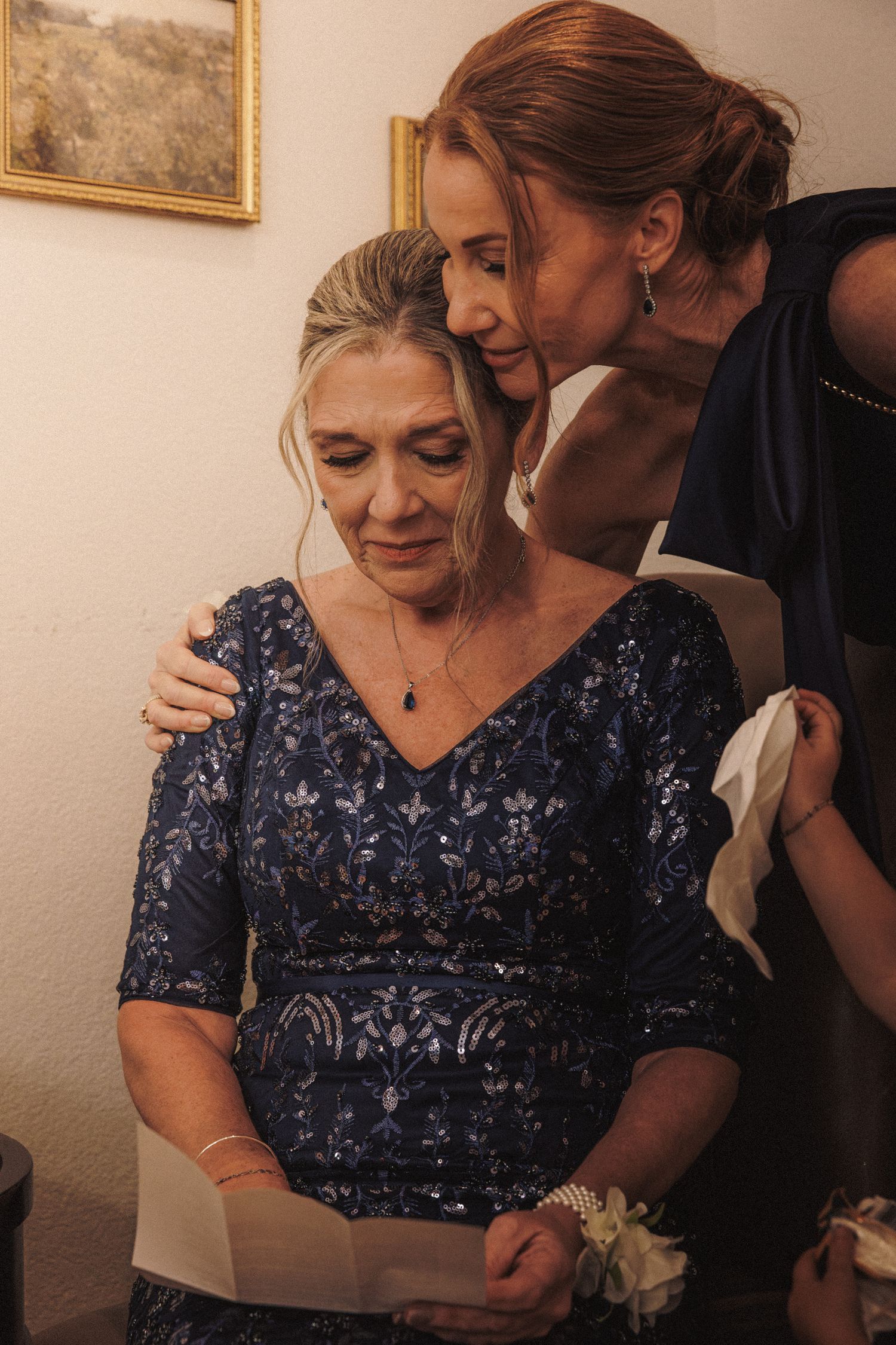 Two women in navy blue dresses sharing emotional moment reading letter at wedding.