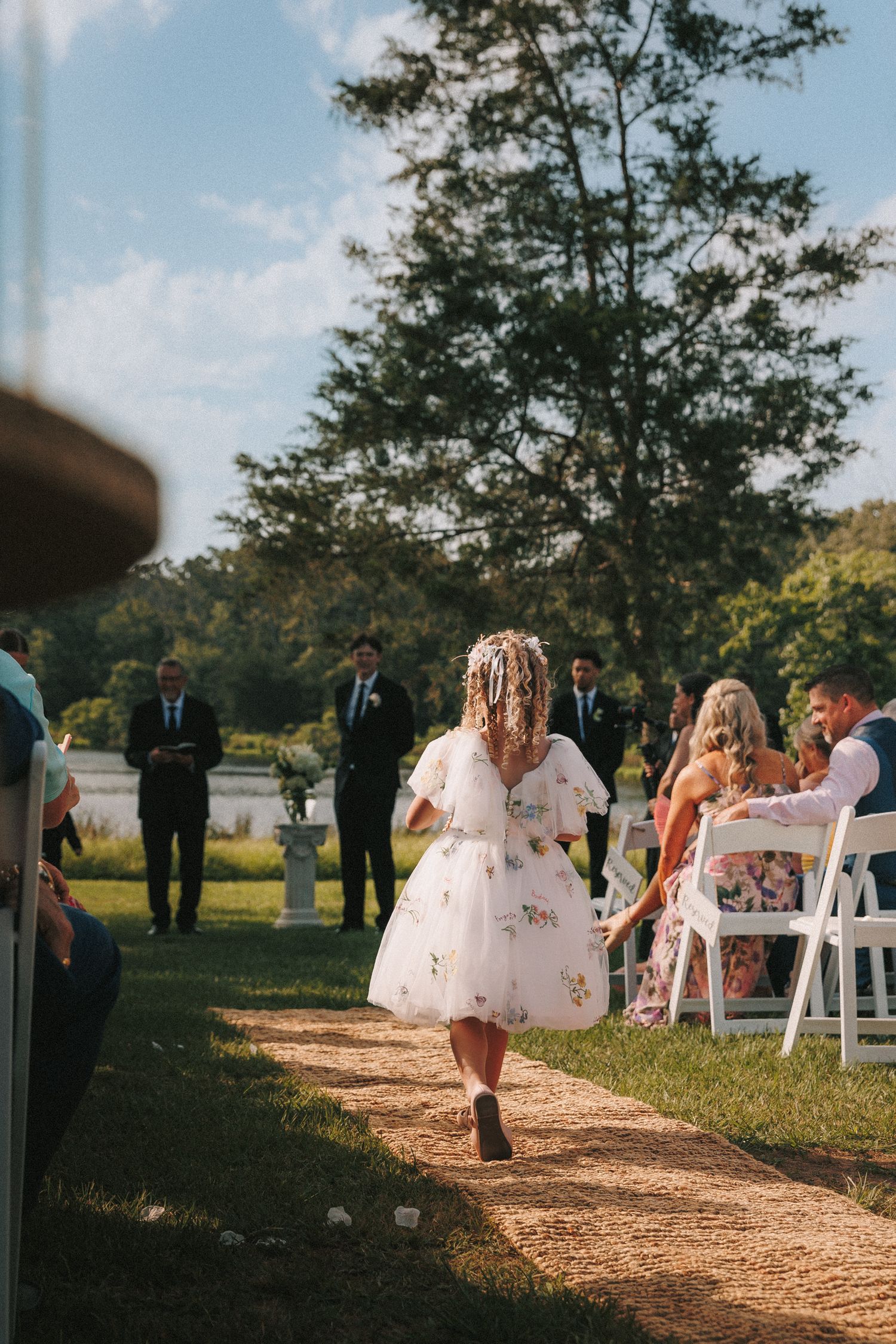 Outdoor wedding ceremony setup with white chairs along a dirt path under trees.