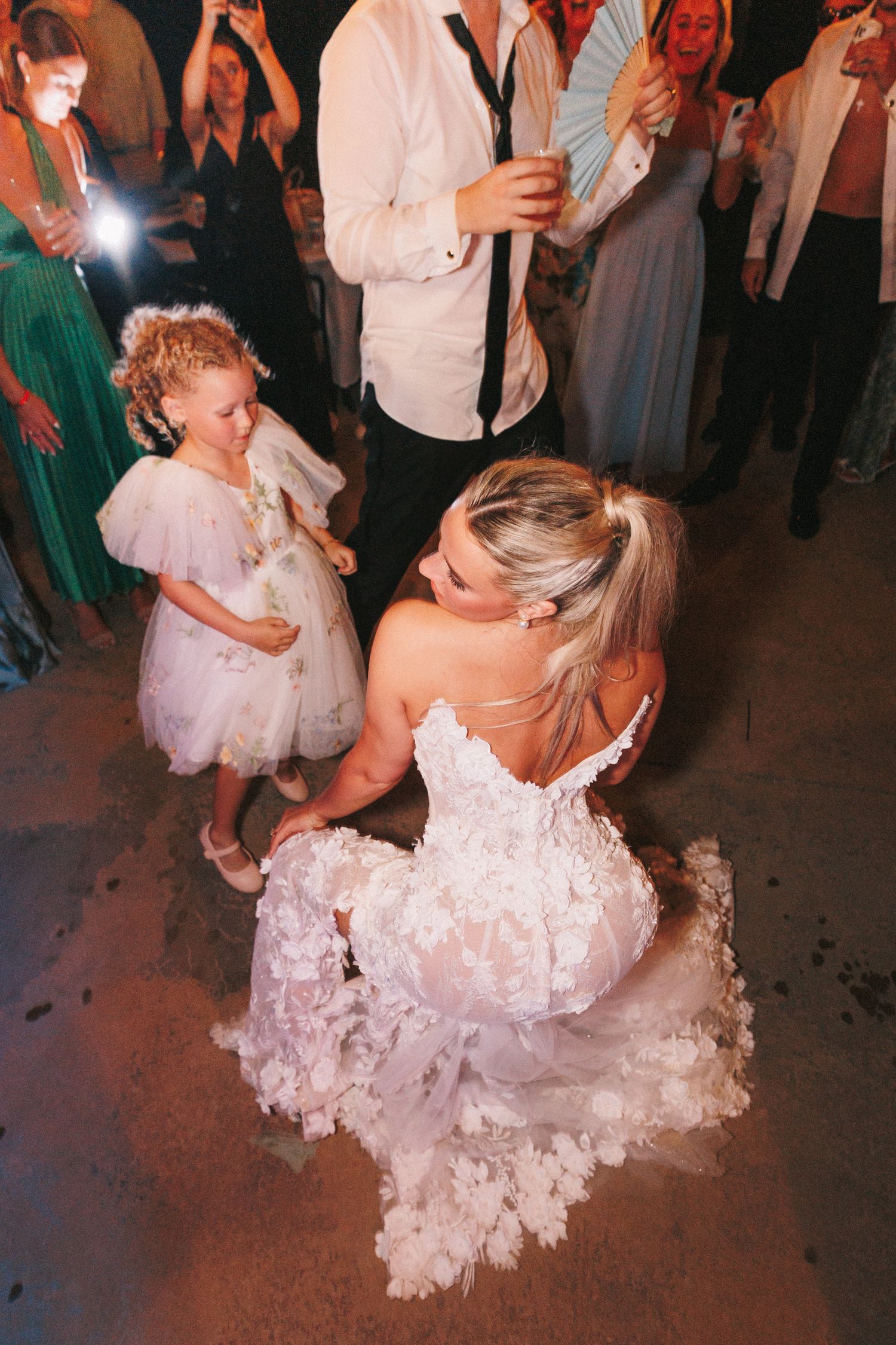 Wedding guests dancing together on a dark dance floor illuminated by ambient lighting.