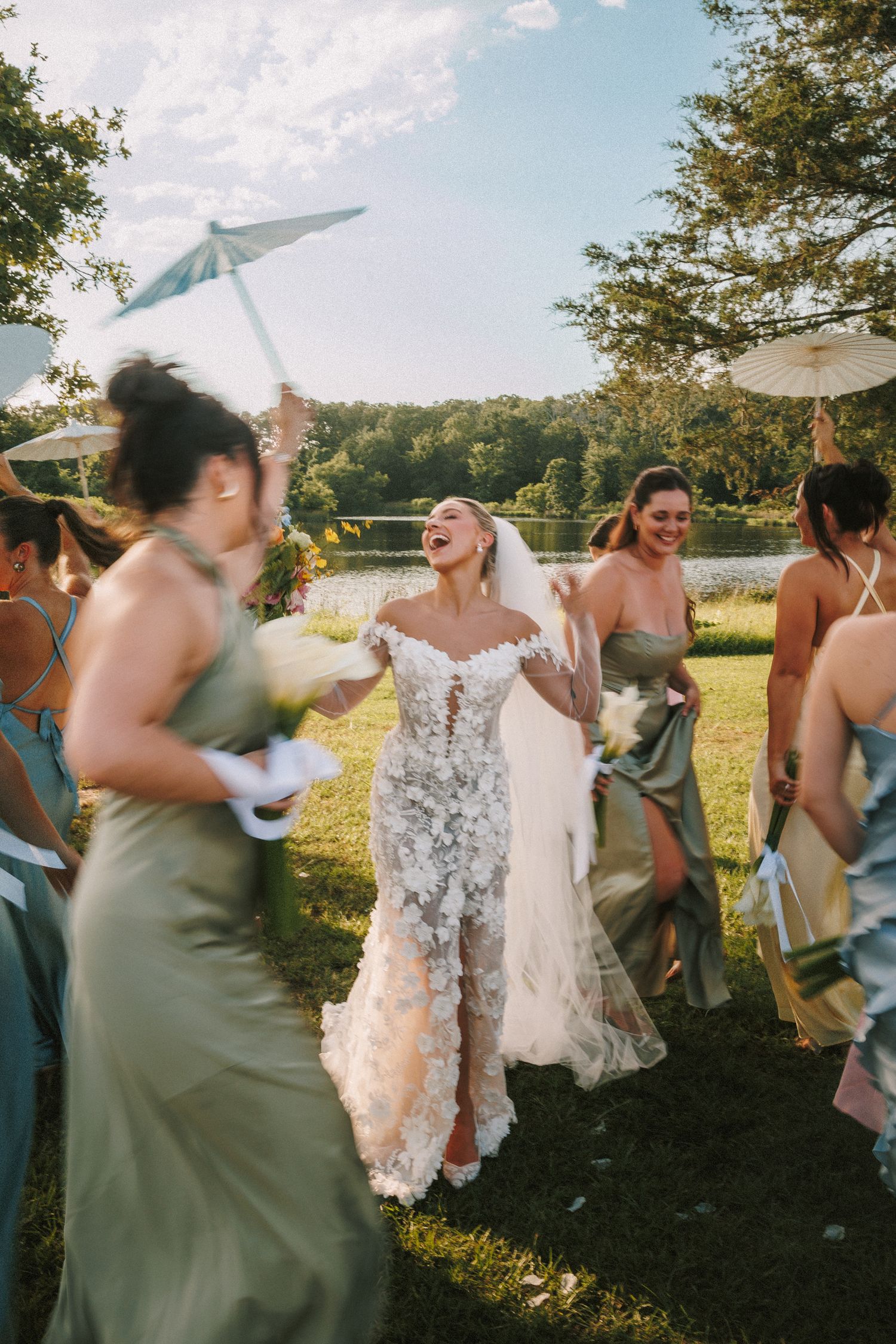 Bridesmaids in sage green dresses dancing together during an outdoor wedding celebration.