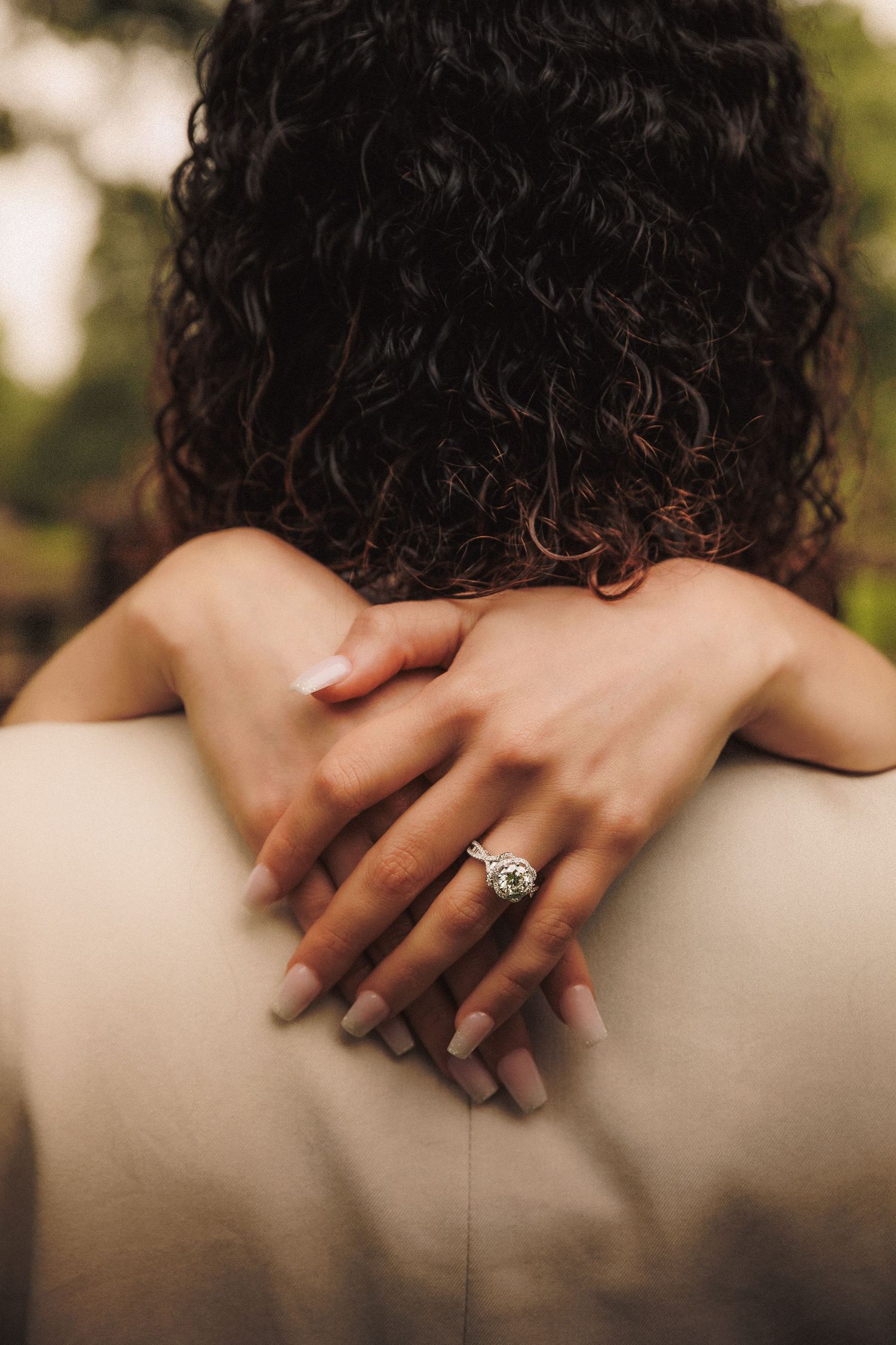 A close-up sequence of hands with curly hair showing a sparkling engagement ring in natural outdoor lighting.