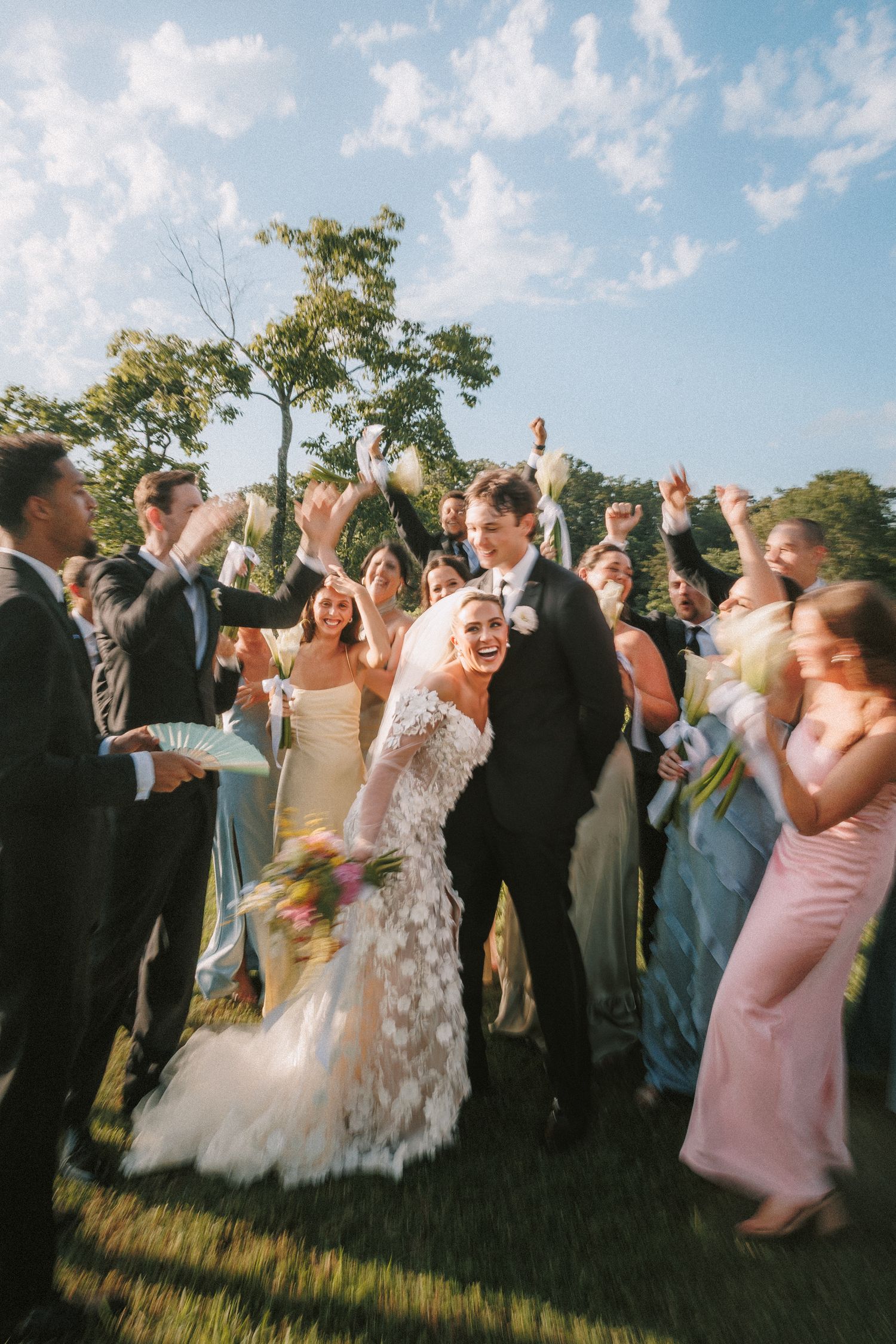 A joyful wedding celebration outdoors as newlyweds walk through cheering guests on a sunny afternoon.