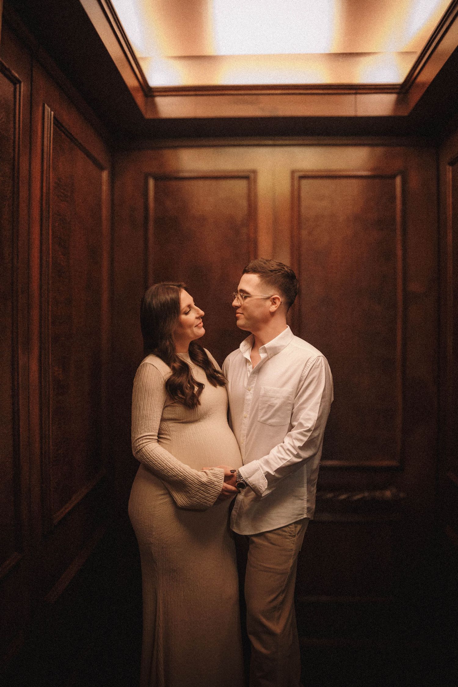 A couple embraces in a warmly lit wooden-paneled room during an intimate photoshoot.