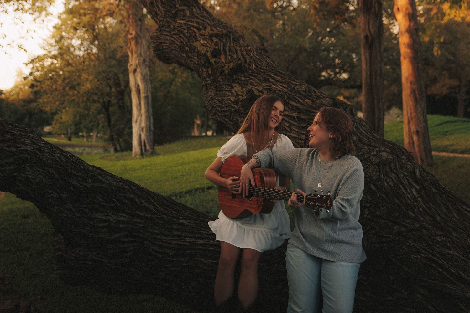 A couple enjoys a tender moment together near a large tree during sunset.