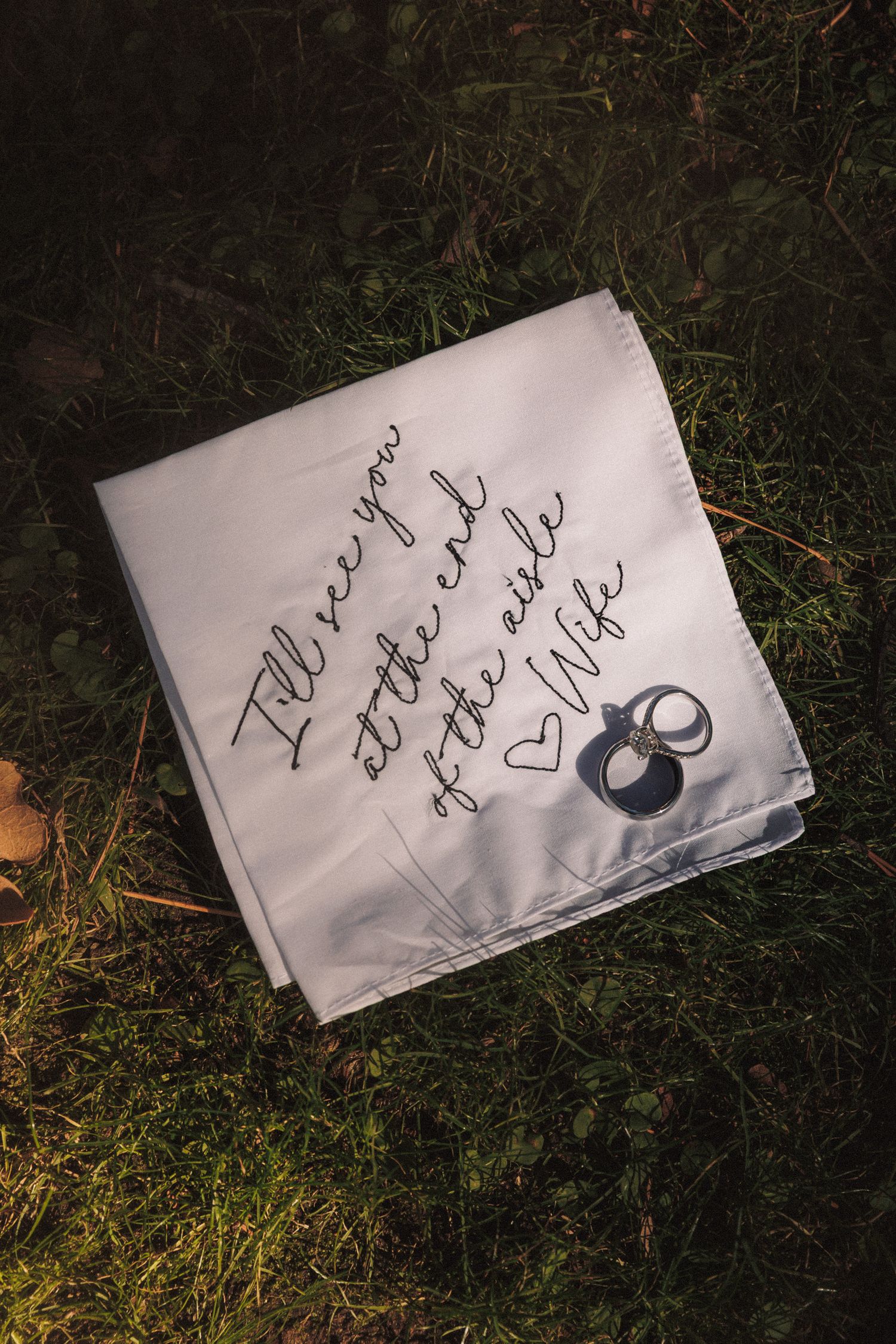 Embroidered wedding handkerchief reading I'll see you at the end of the aisle Wife with two wedding rings on grass.