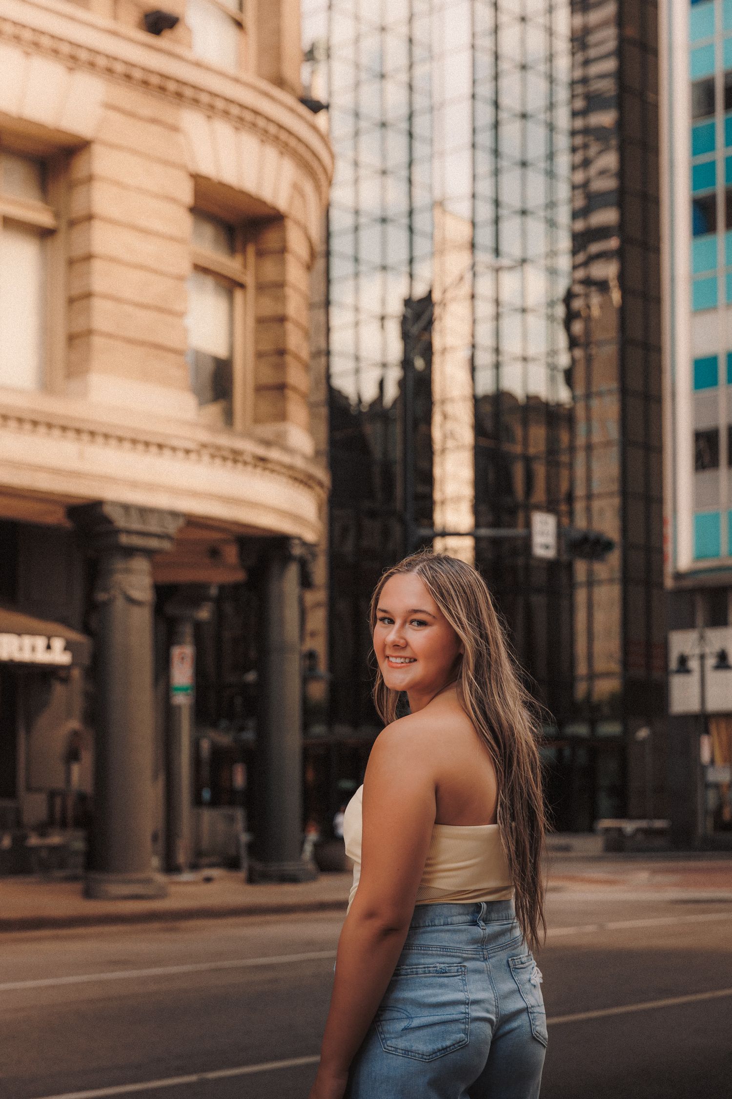 Urban street scene with person in blue jeans against backdrop of modern buildings at sunset.