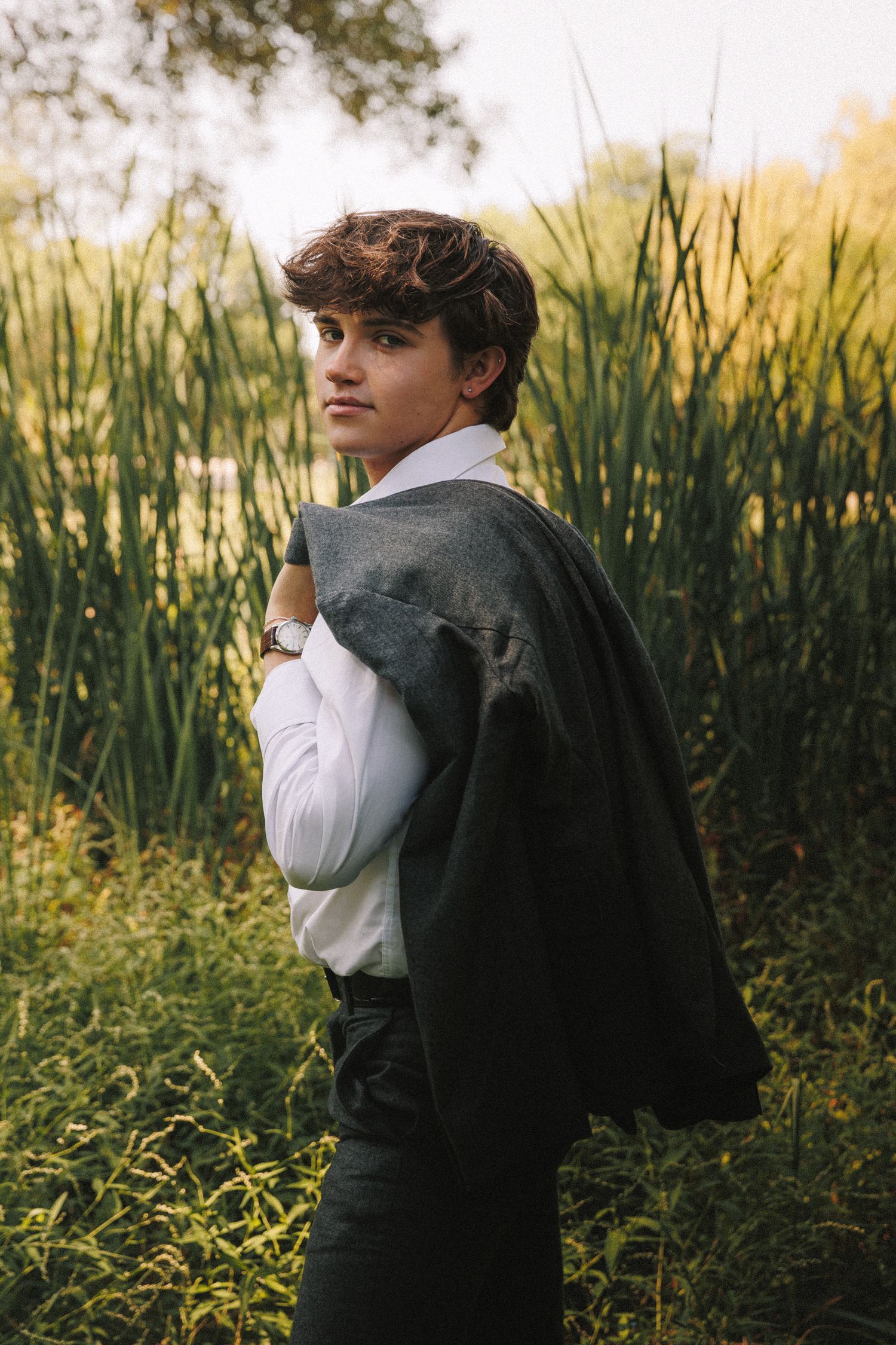 Person in casual attire stands in a field of tall grass and yellow flowers during golden hour.
