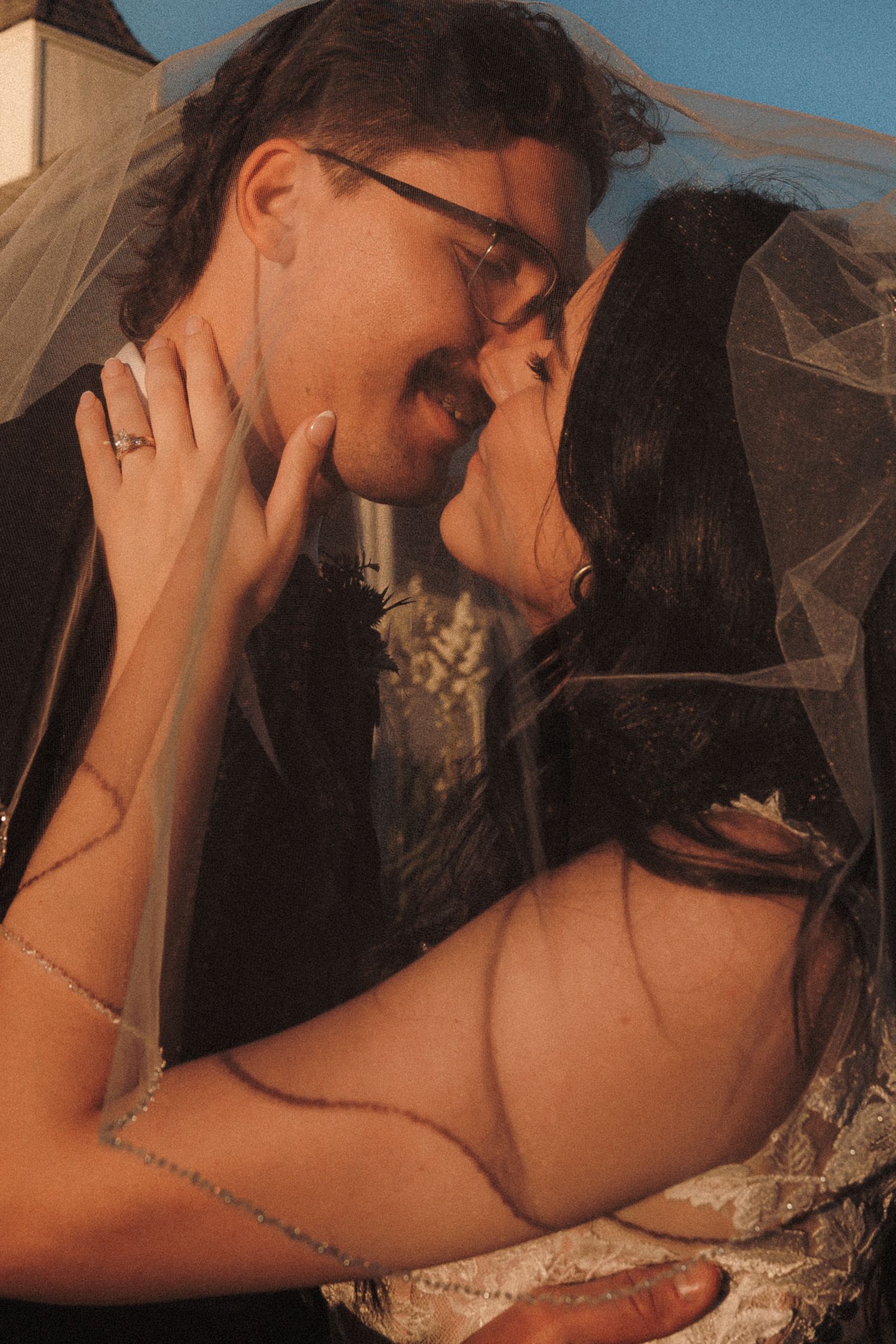 Bride and groom sharing romantic moment under wedding veil with warm sunset light behind them.