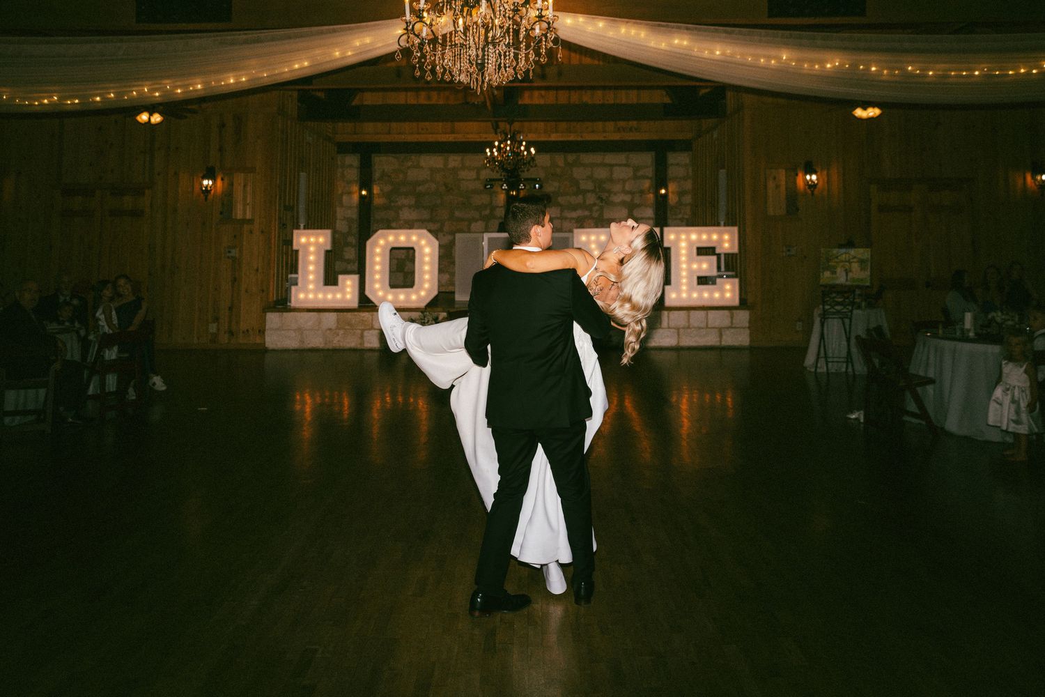 Bride and groom sharing first dance before illuminated LOVE sign on wedding dance floor.