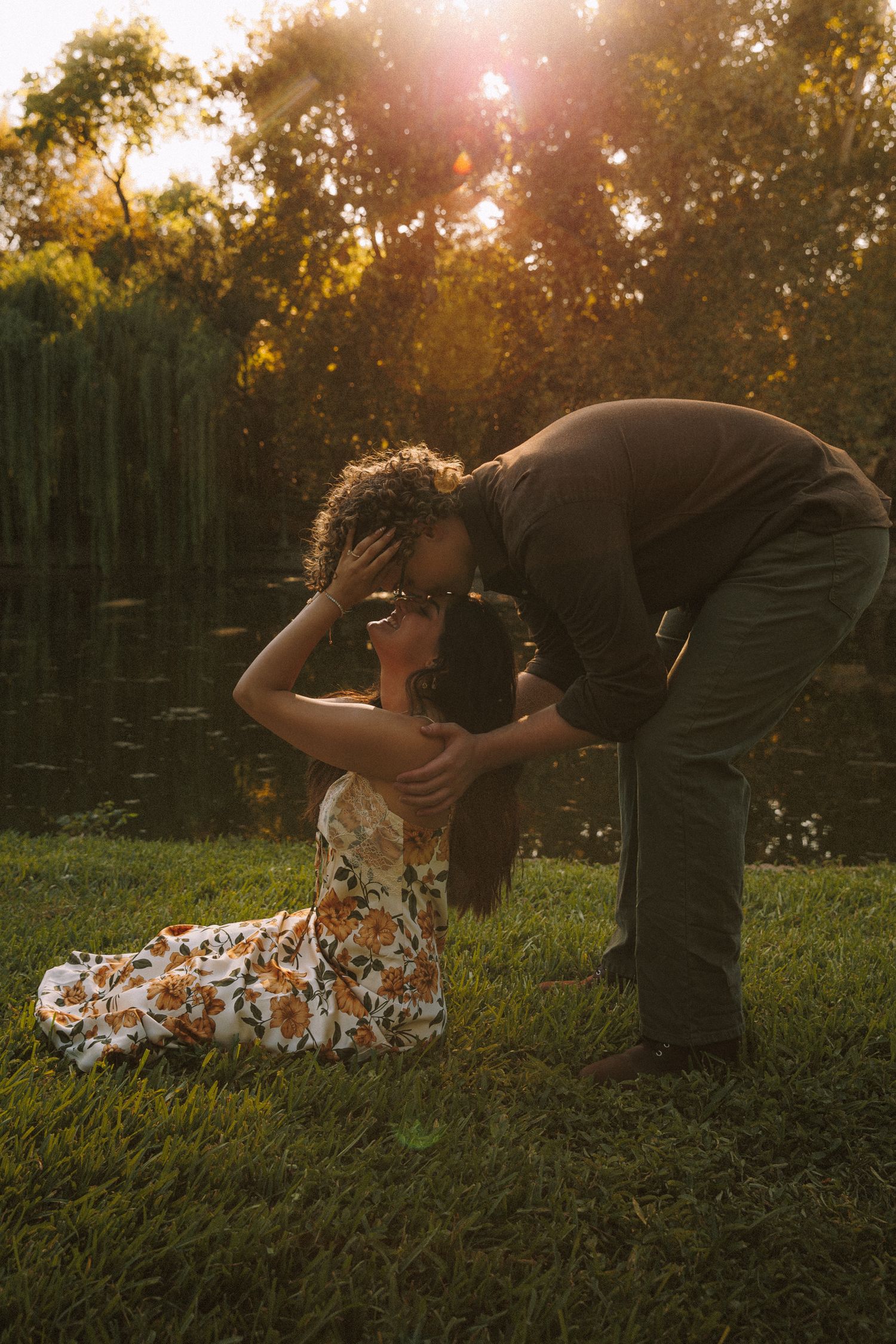 Romantic couple embraces on grassy field during golden sunset with sun flare in background.
