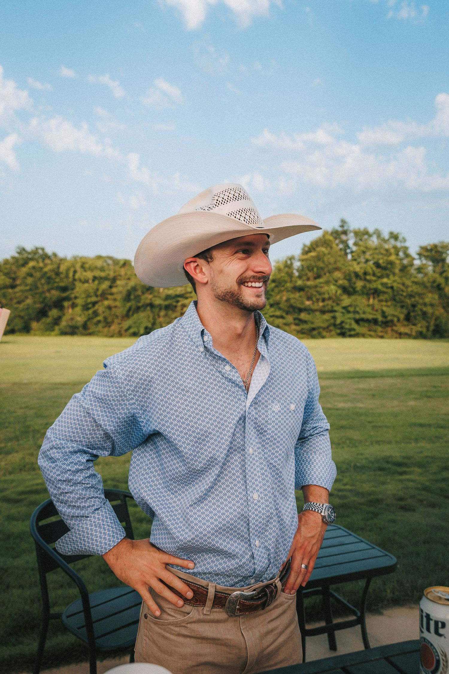 Guest in cowboy attire laughing while sitting outdoors during a country-style wedding.