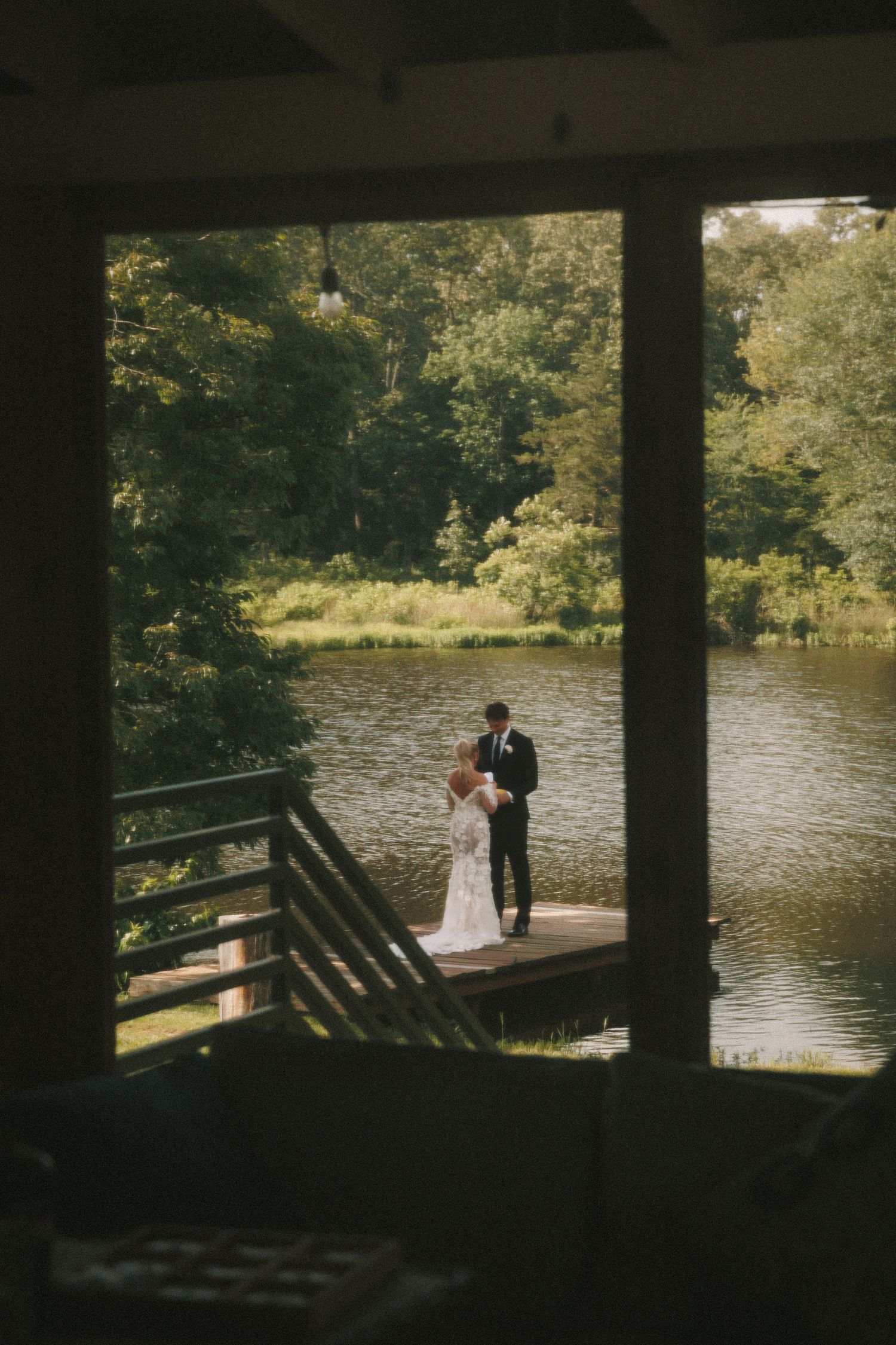 Wedding couple photographed through window frame on lakeside dock.