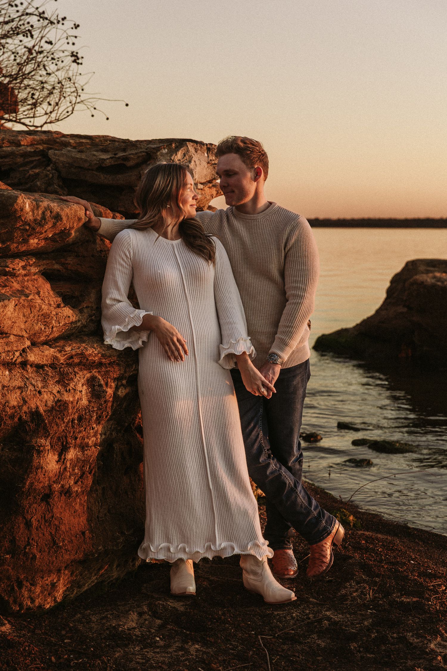 A couple poses together on rocky coastal cliffs during golden hour by the ocean.