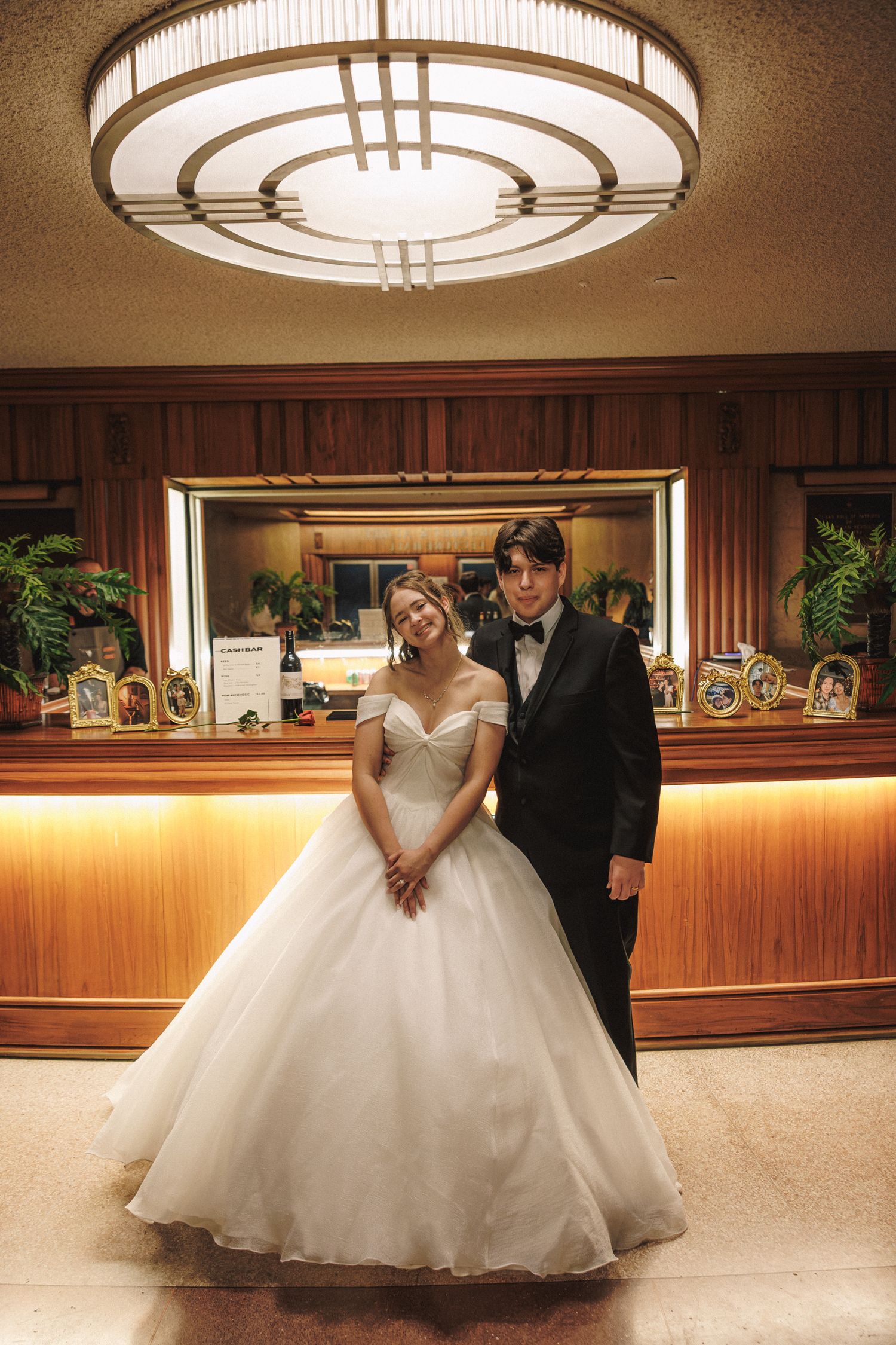 Bride and groom posing together in front of a warmly lit hotel lobby bar counter.