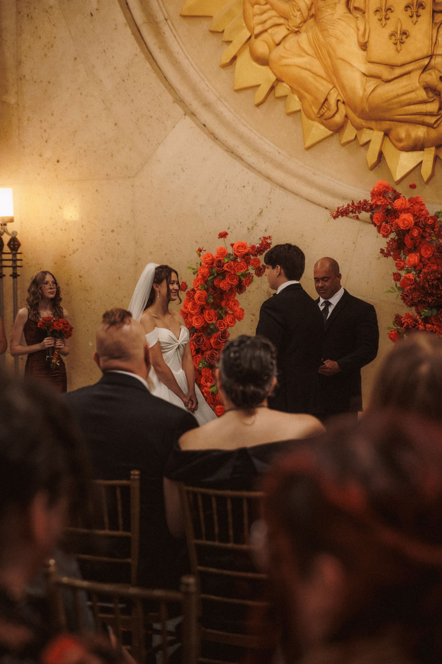 Wedding ceremony with bride and groom at floral arch of red roses in elegant venue.