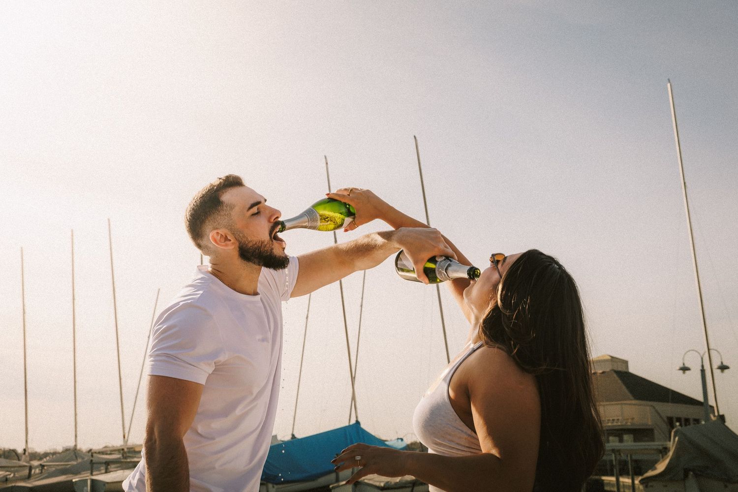 A couple celebrates with champagne at a marina during sunset.