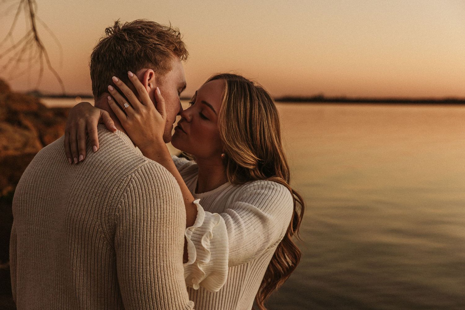 Intimate sunset portrait of couple in cozy sweaters by the water.