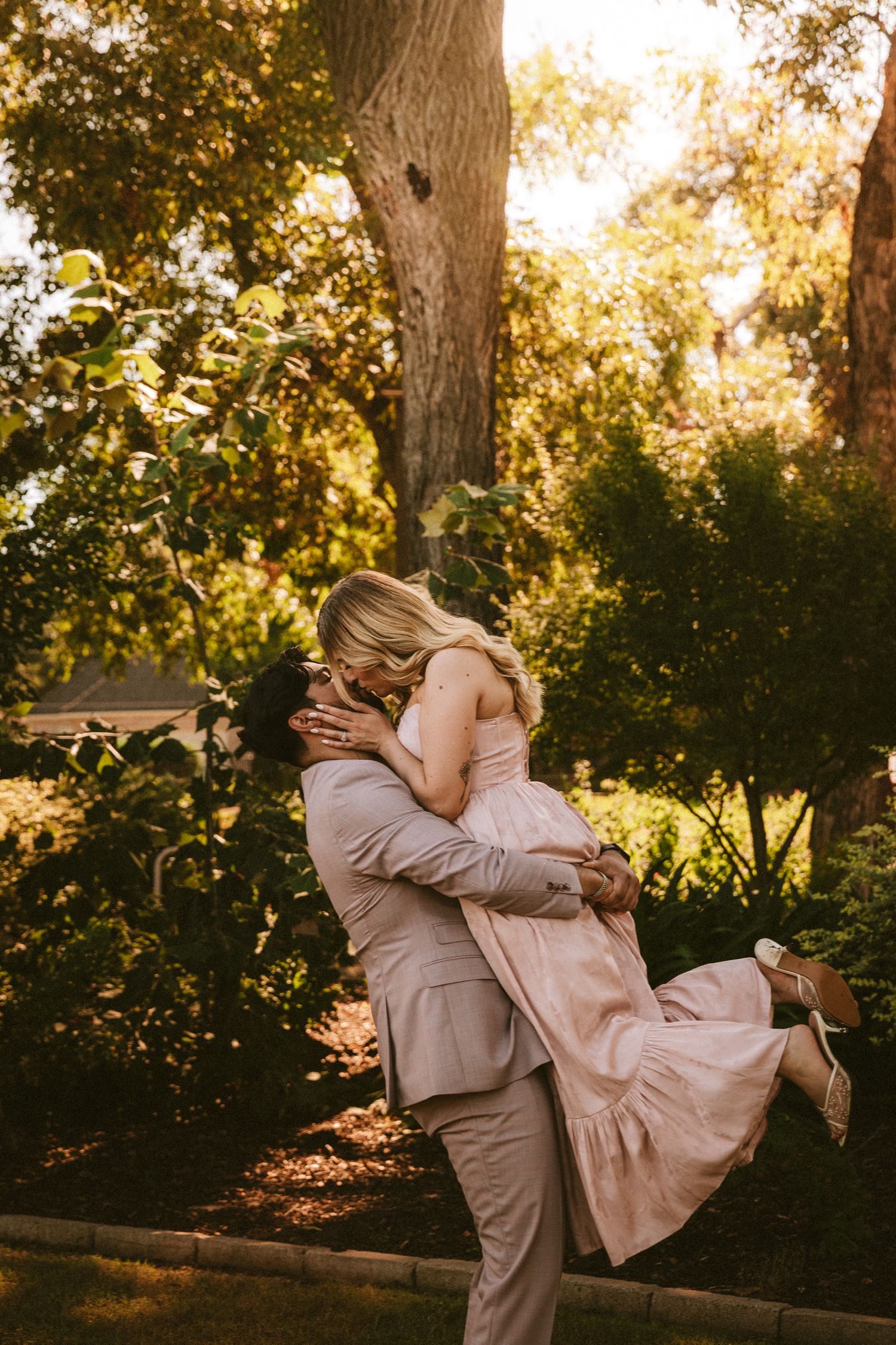 A joyful lift pose captured in warm sunset lighting among garden trees.