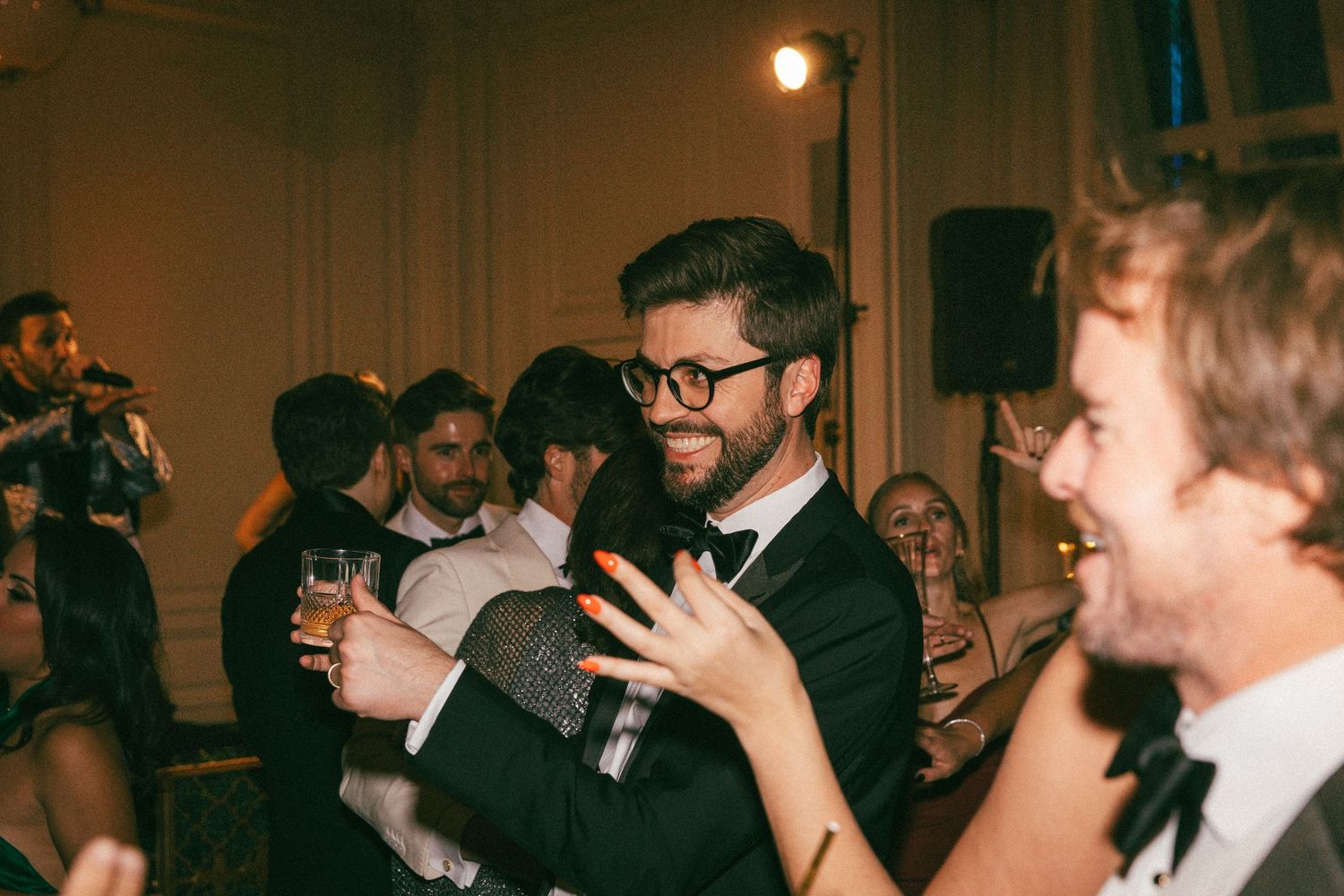 A wedding guest in glasses and bow tie dances joyfully at a lively reception.