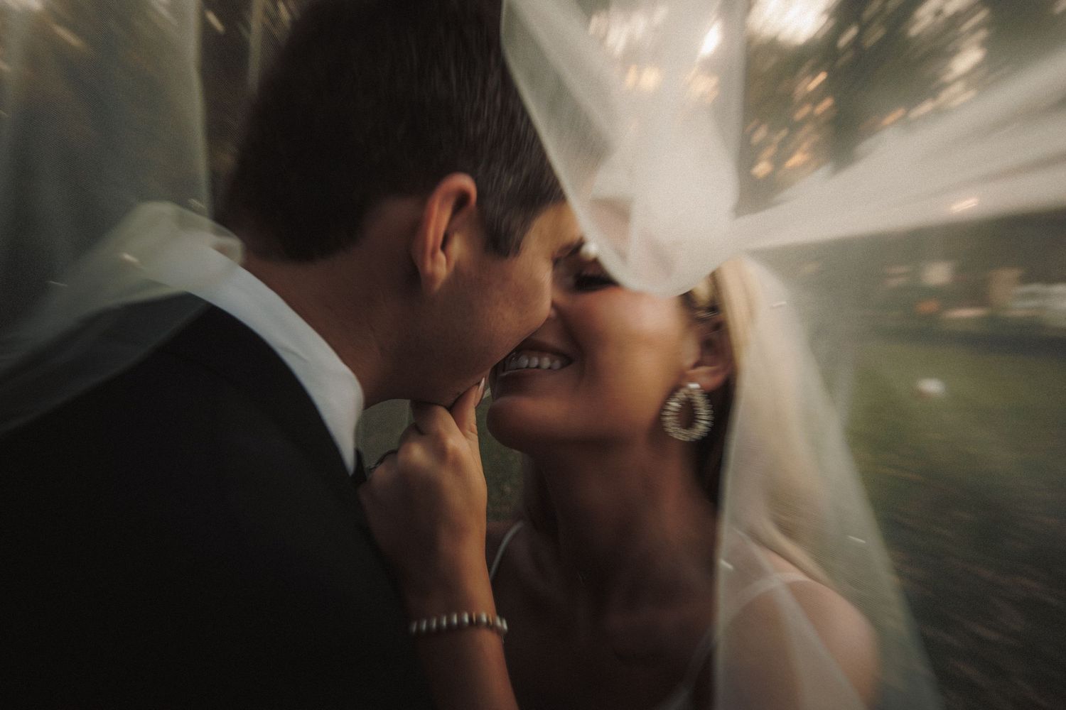 Romantic close-up of bride and groom almost kissing under a flowing wedding veil.