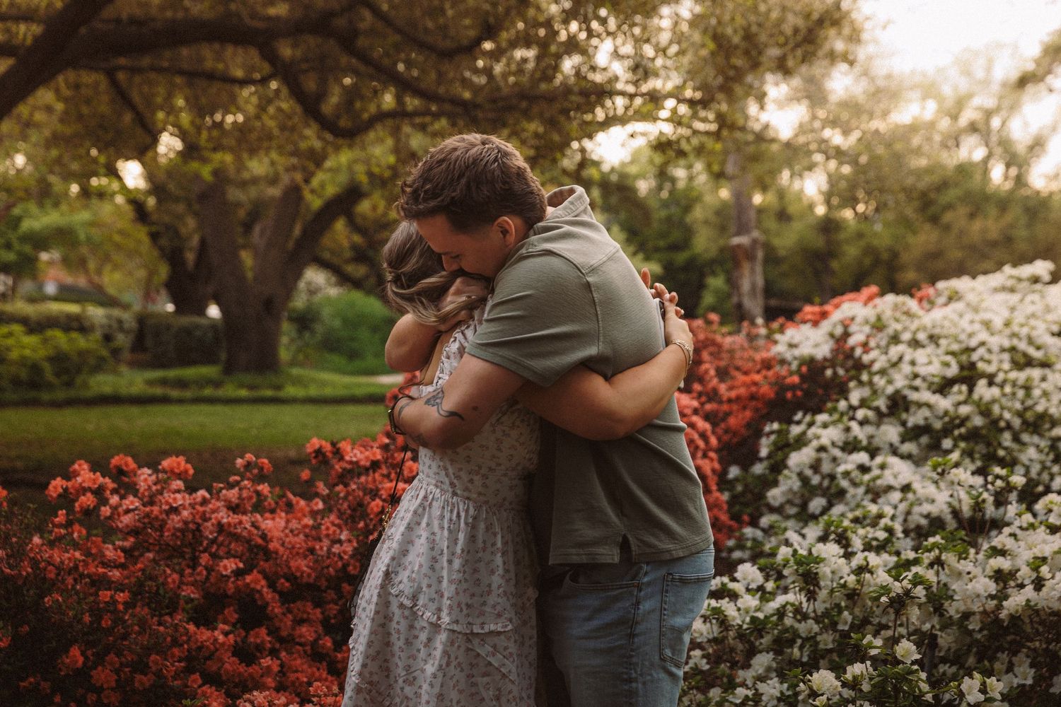 A couple shares a tender embrace surrounded by vibrant red and white flowering bushes.