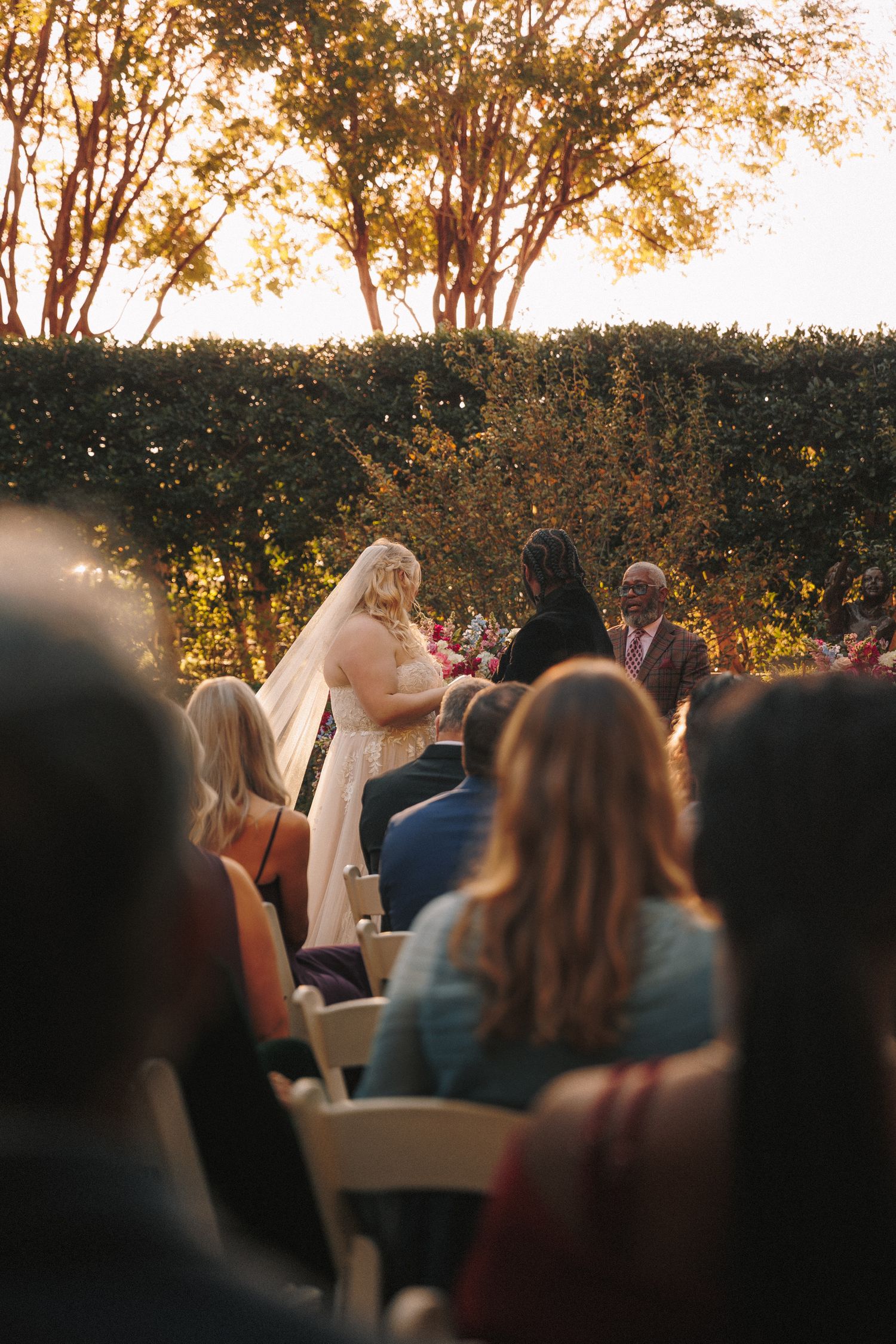 Outdoor wedding ceremony at sunset with bride and groom at altar before seated guests.
