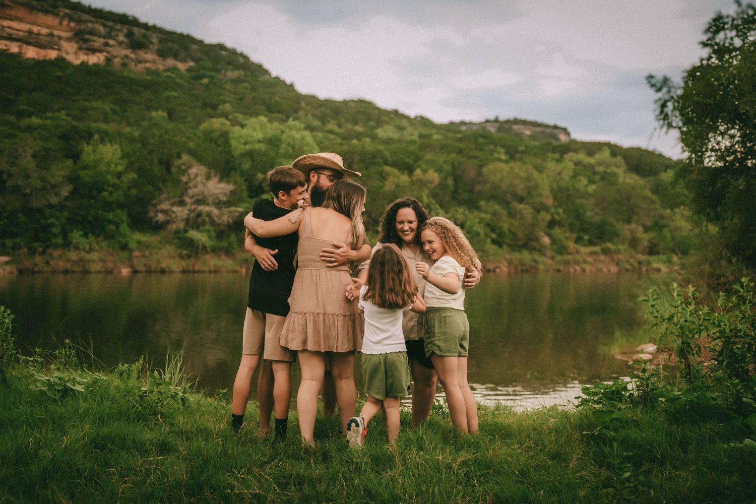Group celebration photoshoot against a backdrop of green hills and peaceful lake waters.