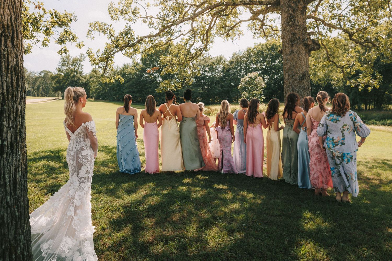 Wedding party gathered outdoors in pastel dresses and formal attire during golden hour.