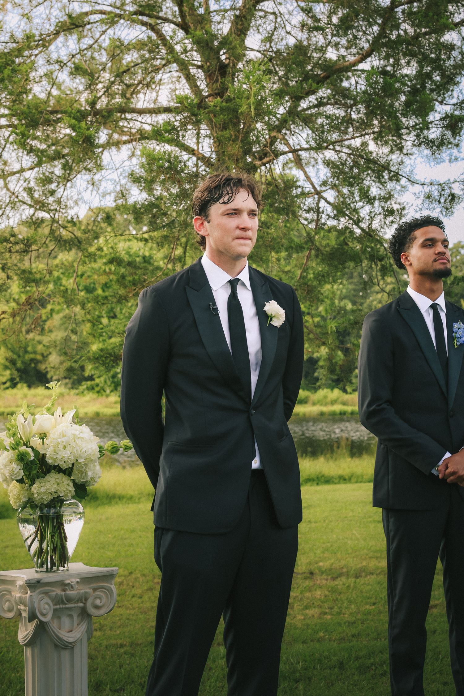 Groomsmen in black suits stand at attention during outdoor ceremony.