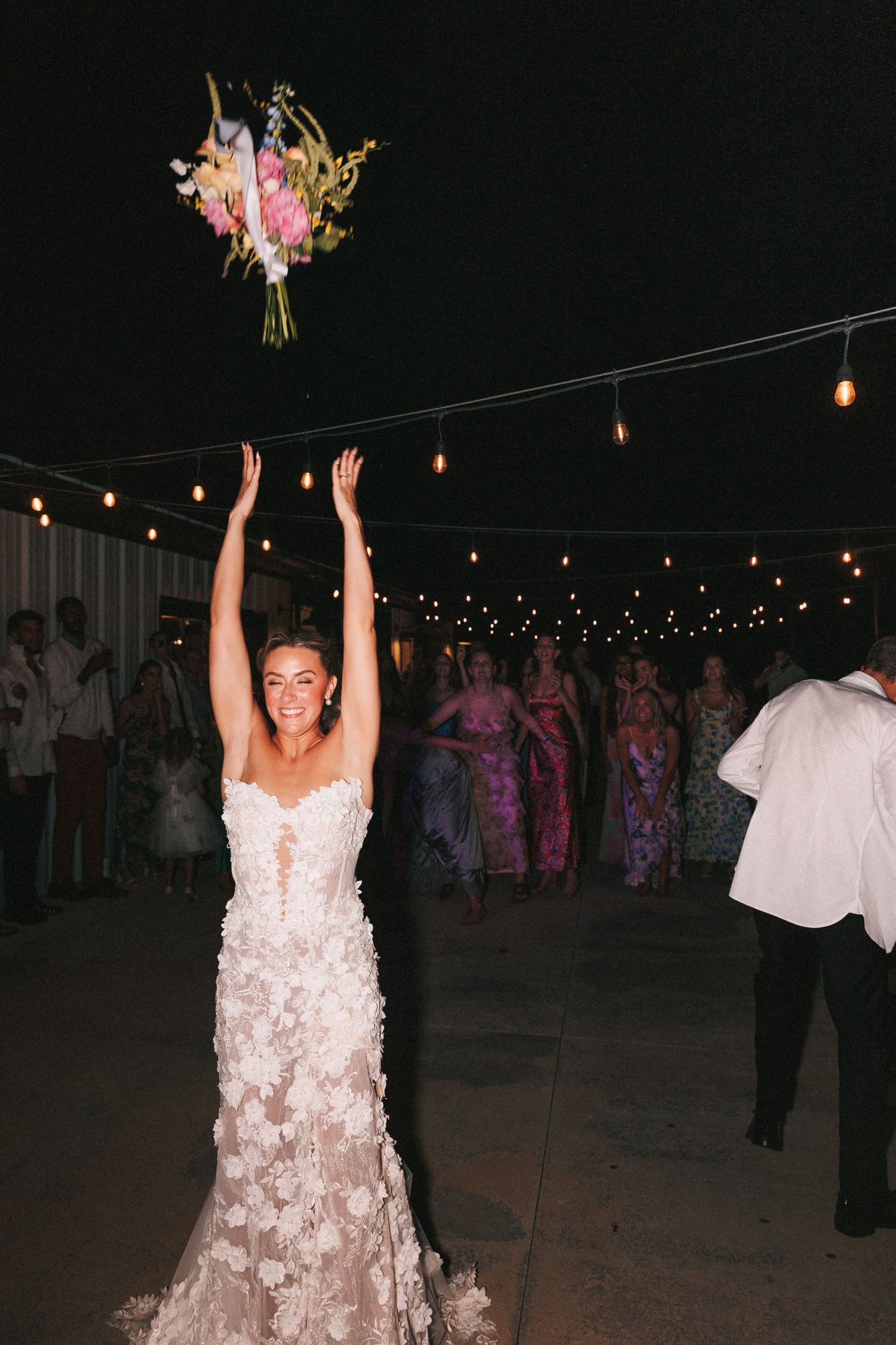 A nighttime outdoor celebration with string lights where people dance under starlit sky.