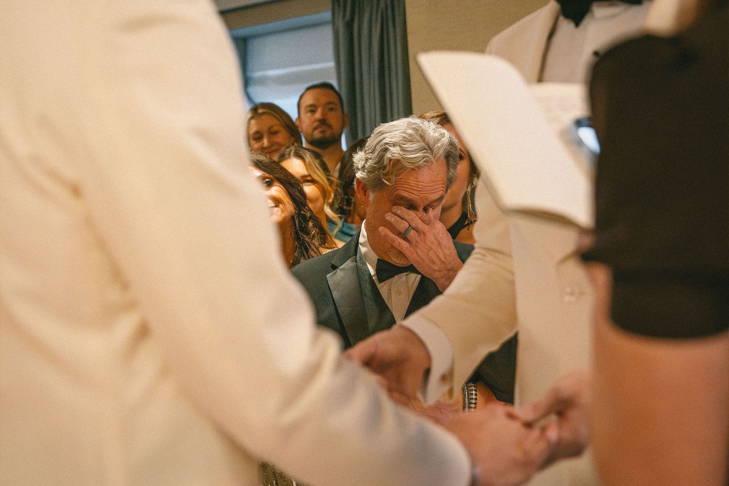 An emotional wedding guest covers his face with his hand during a heartfelt ceremony.