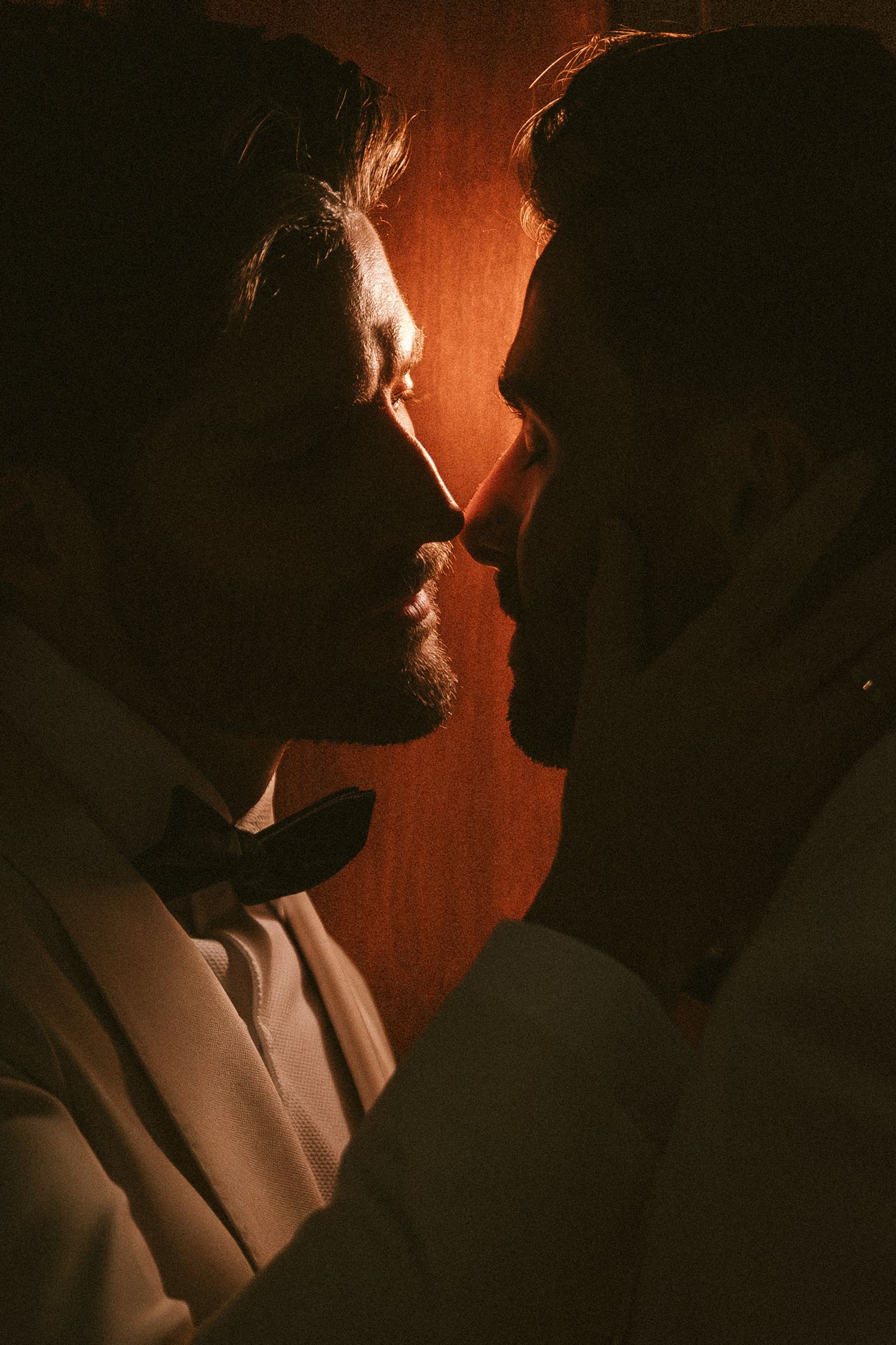Romantic silhouette of two grooms facing each other closely, bathed in warm amber light before their wedding.