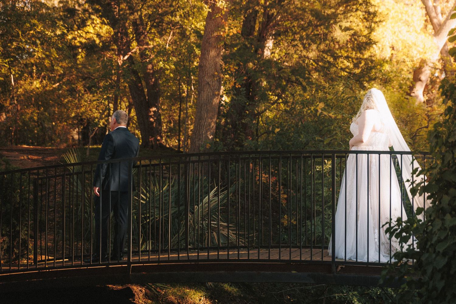Bride and groom sharing a first look moment on a bridge surrounded by lush golden trees.