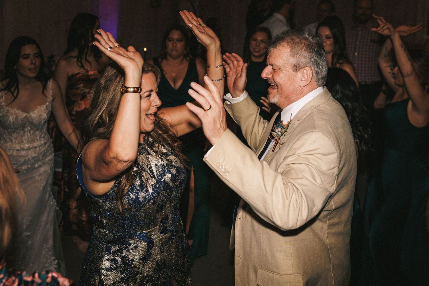A woman in a blue dress and older man in a tan suit dance joyfully together at a wedding reception.
