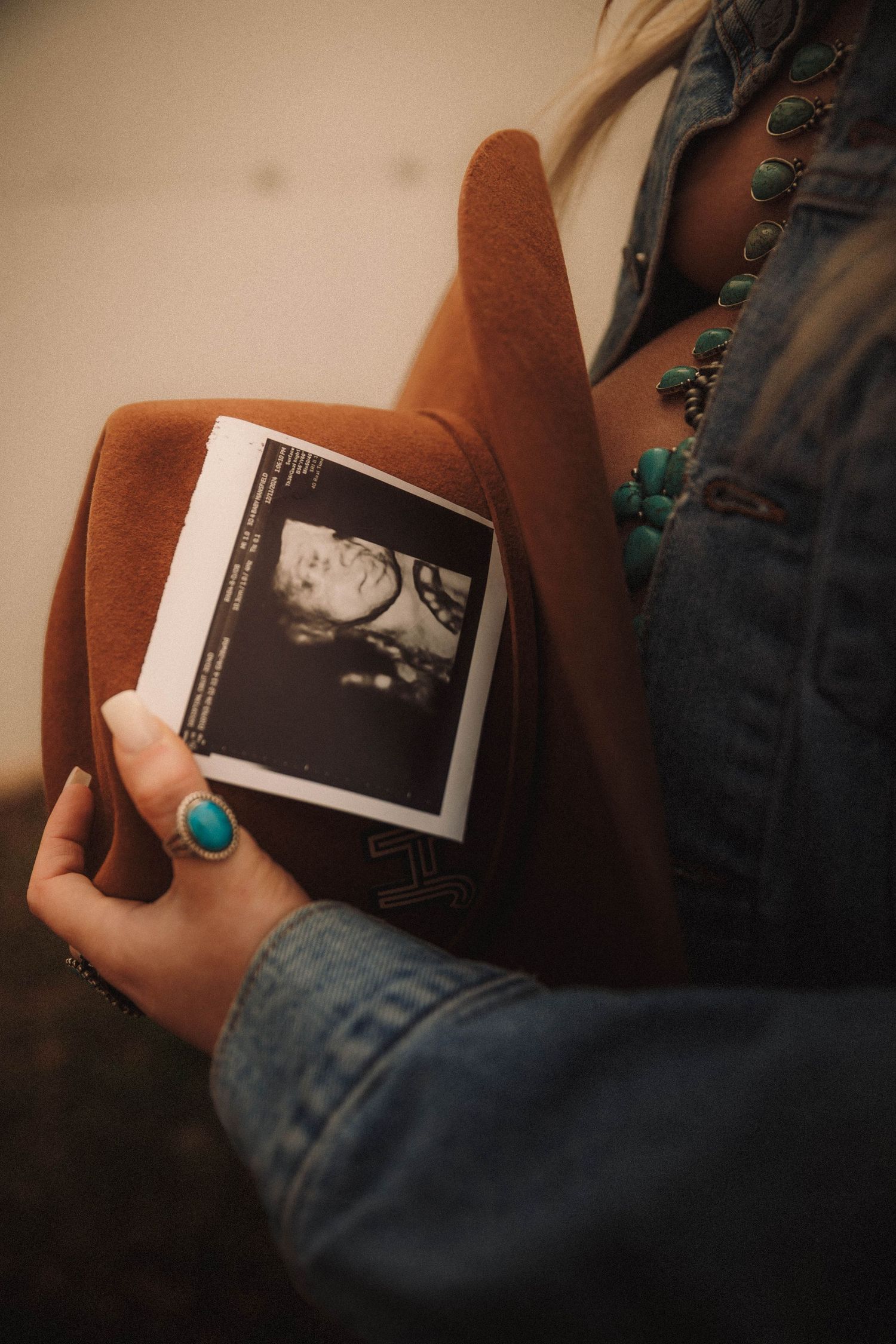 A series of ultrasound scan photos being held against a denim background with turquoise jewelry visible.
