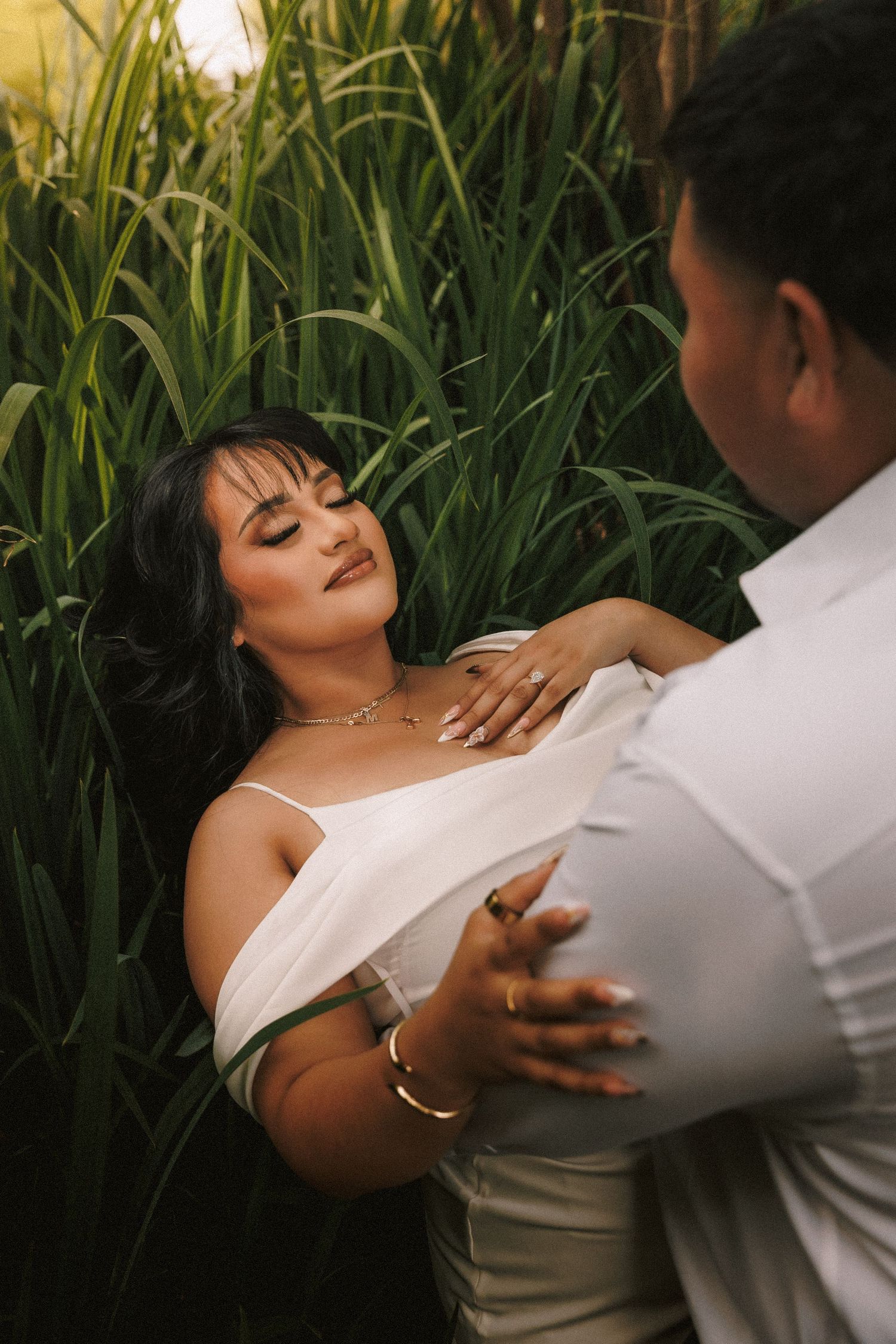 A couple shares an intimate moment among tall grass and greenery in an outdoor photo shoot.
