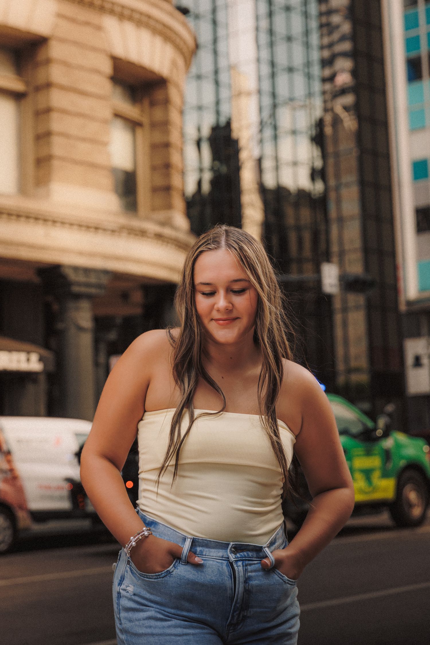 Urban fashion photoshoot featuring casual summer style with cream tank top and denim jeans against city architecture.