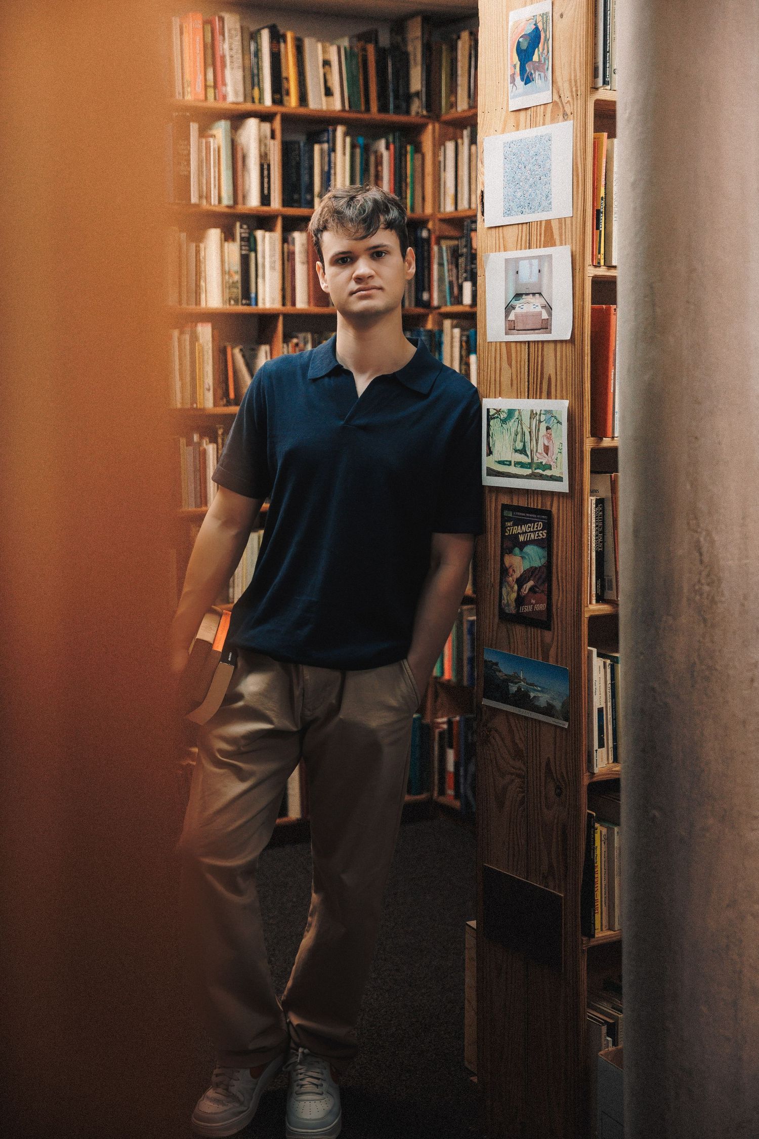 Individual seated in a library with warm lighting and floor-to-ceiling bookshelves in the background.