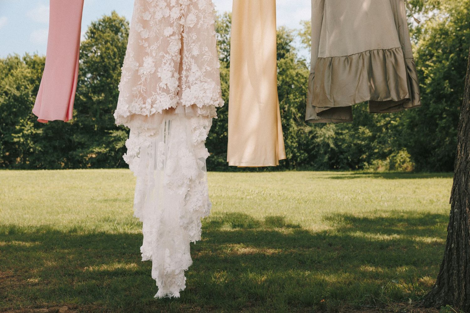 White wedding dresses and formal attire hanging on display against a sunny outdoor backdrop.
