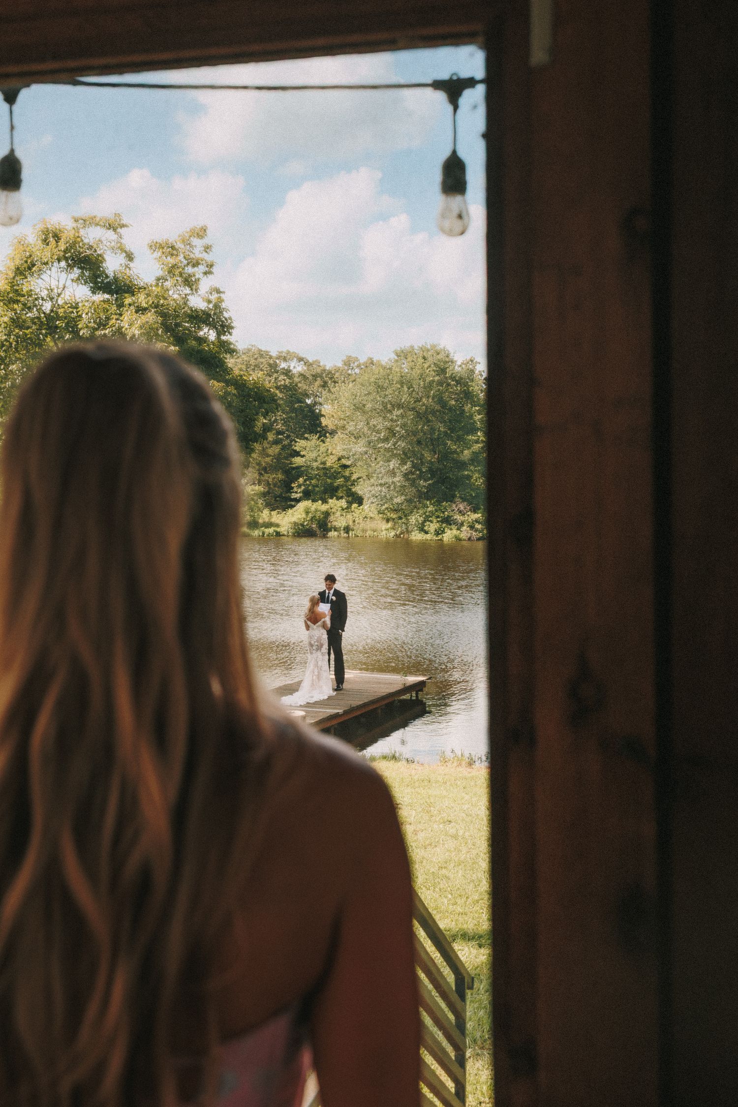 View through a rustic window frame overlooking a lake and outdoor wedding ceremony setting.