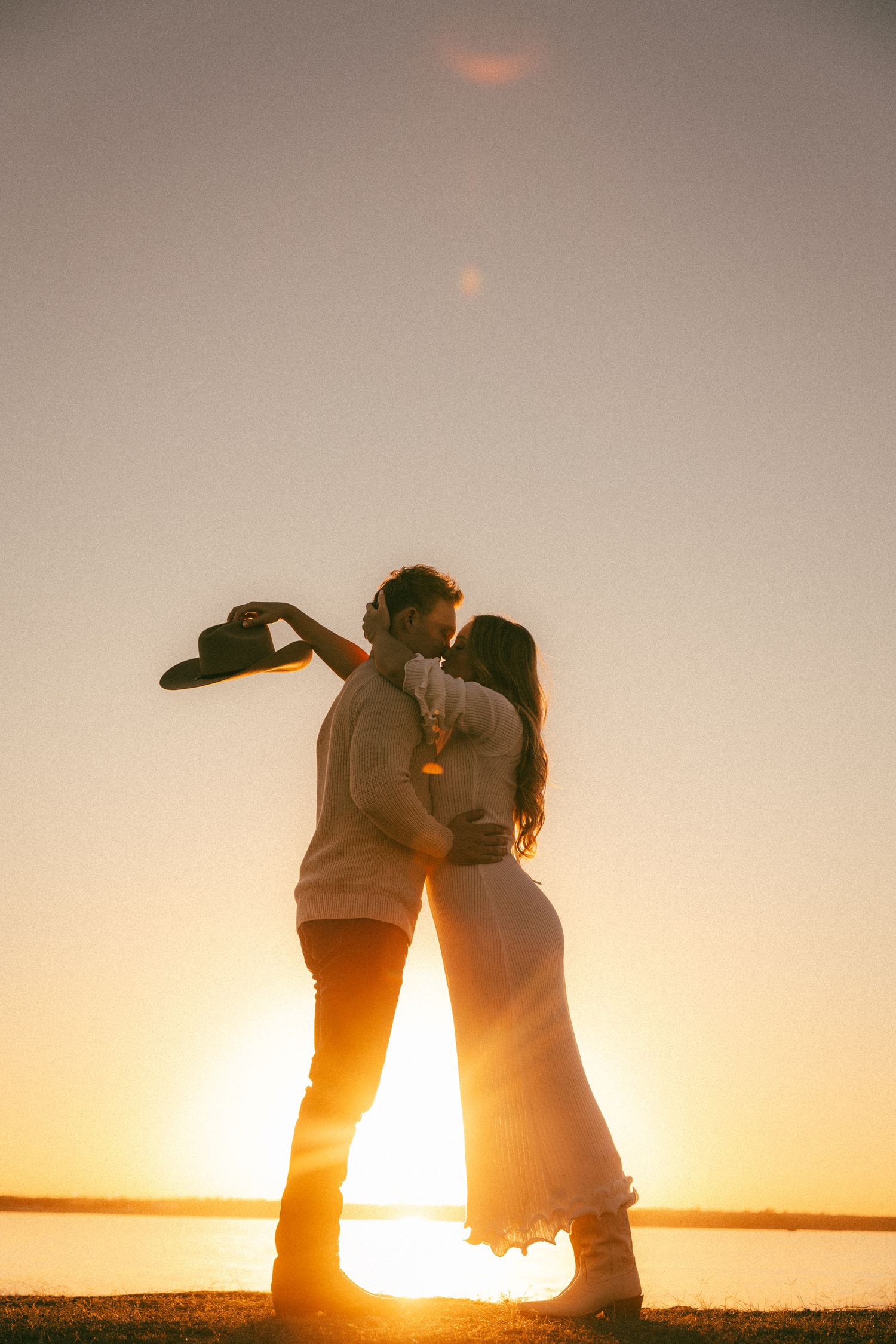 Couple dancing and embracing in dramatic sunset light near a serene lake.