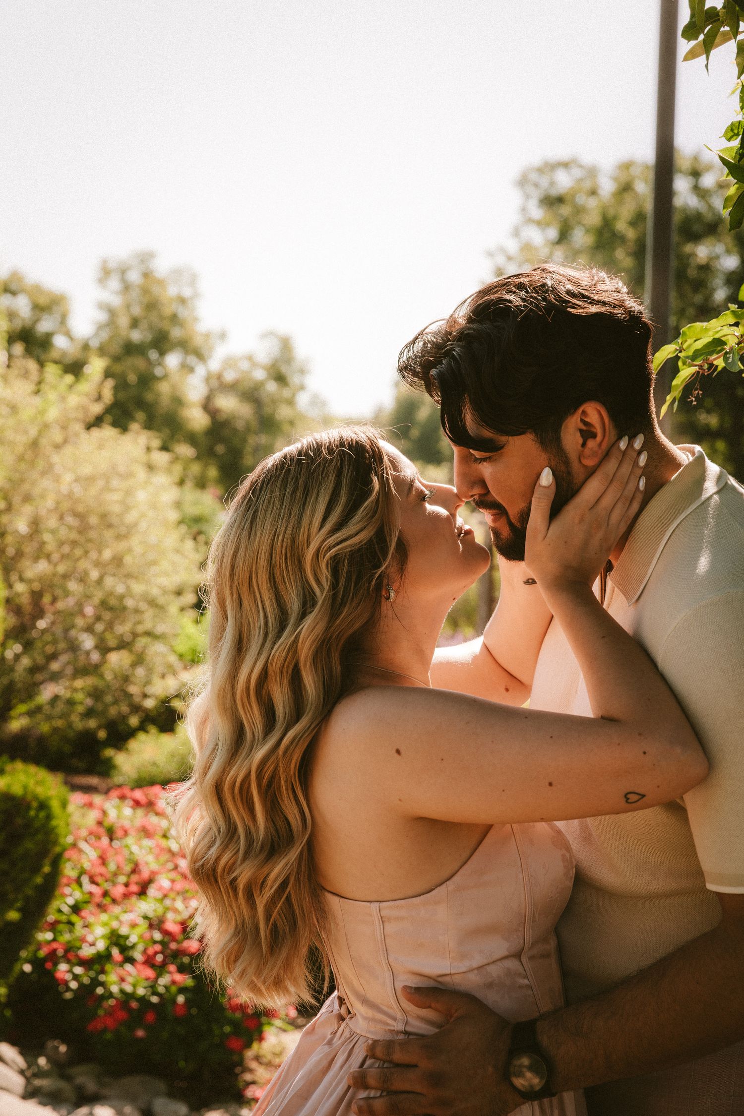 A romantic couple shares an intimate moment in a sunlit garden with blooming flowers.