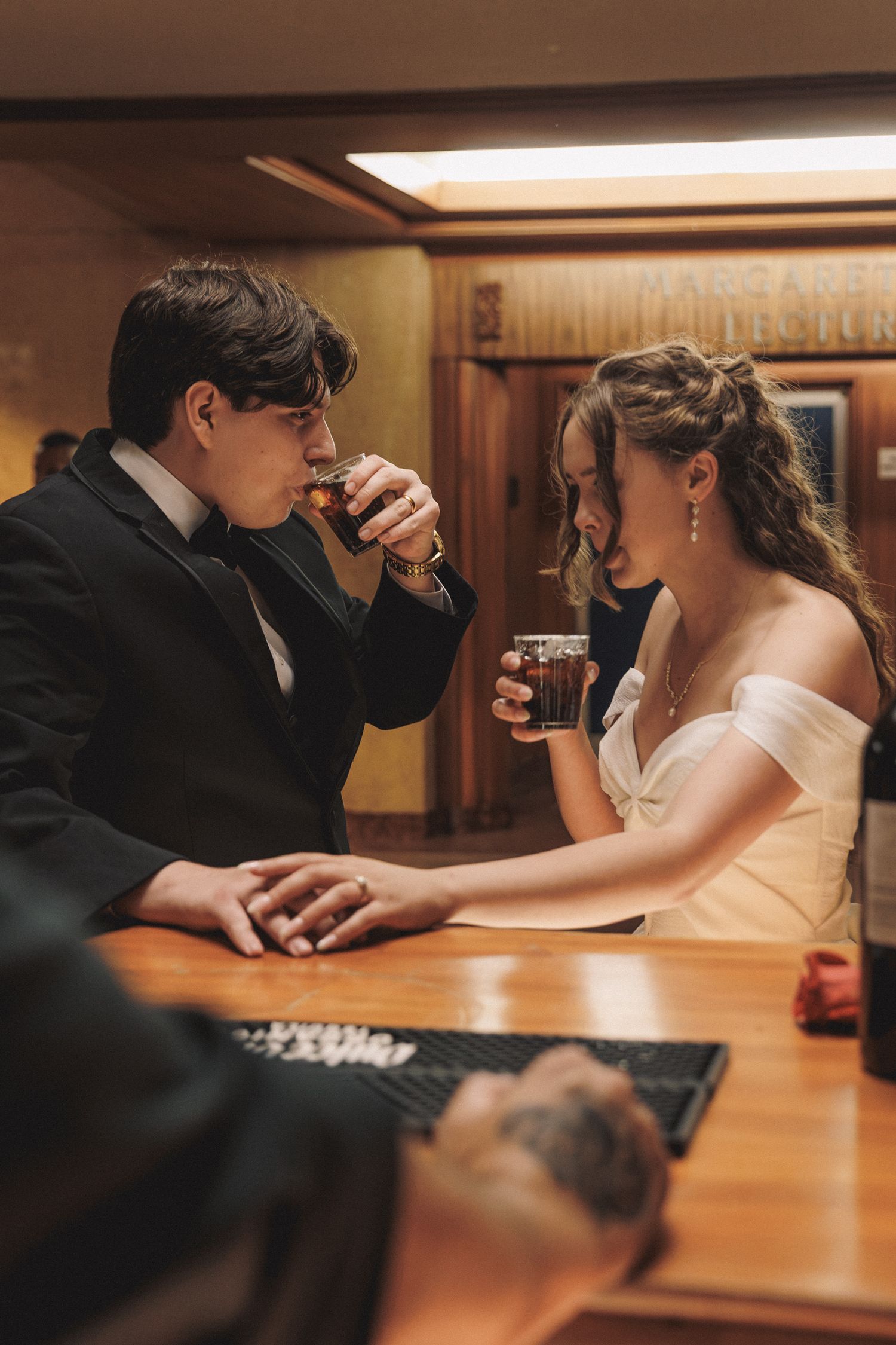 Bride and groom sharing intimate moment drinking whiskey together at wooden bar.