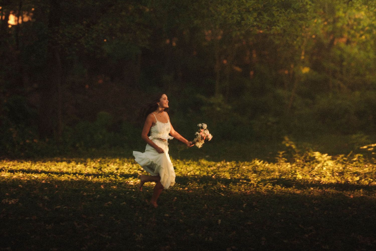 A couple walks through a golden sunlit meadow during sunset while holding hands and enjoying a romantic moment together.