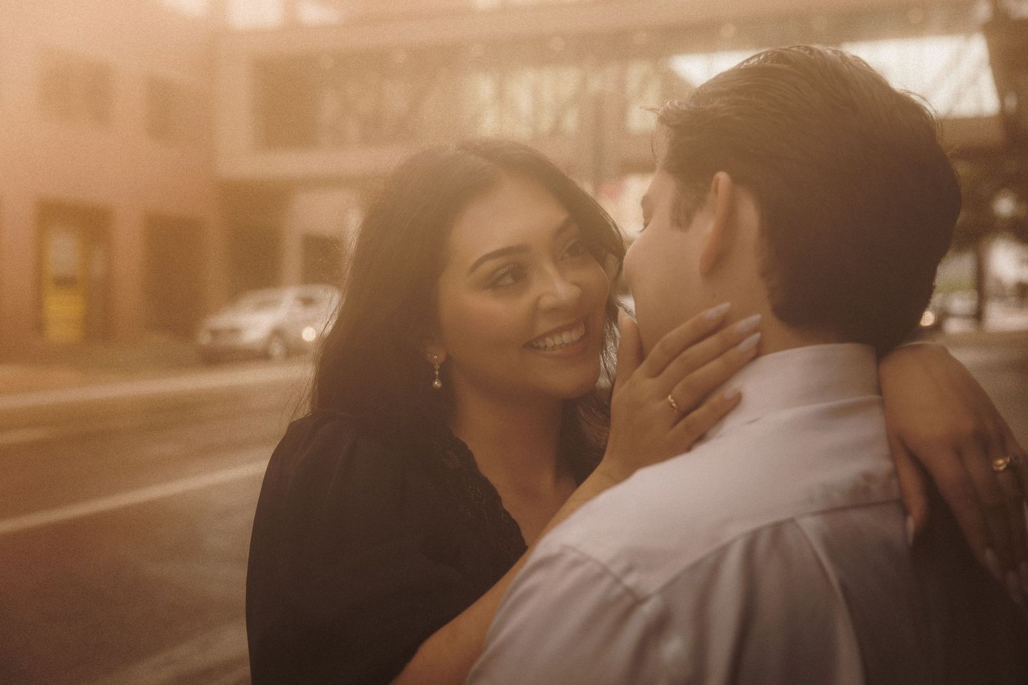 Couple sharing a romantic embrace outdoors at golden hour, woman smiling warmly in a black top.
