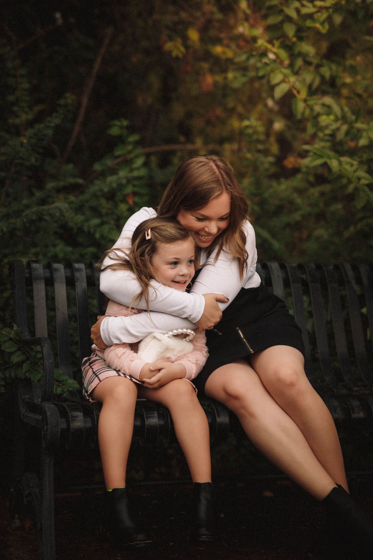 Two people share an intimate moment sitting on a fence in a dark forest setting with dramatic lighting.