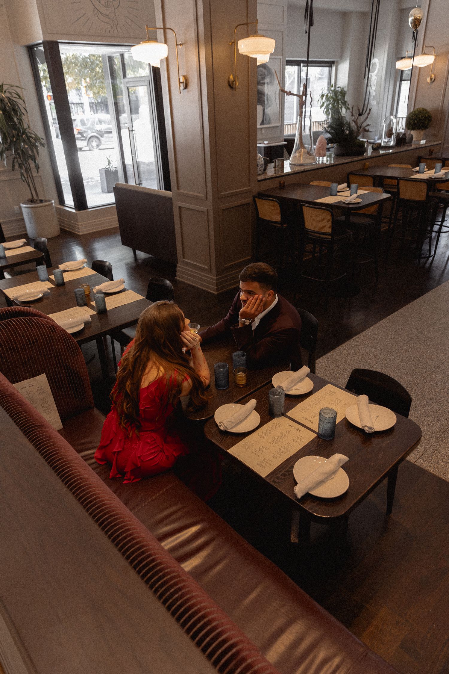 Couple dining at an elegant restaurant, woman in red dress seated across from man in suit.