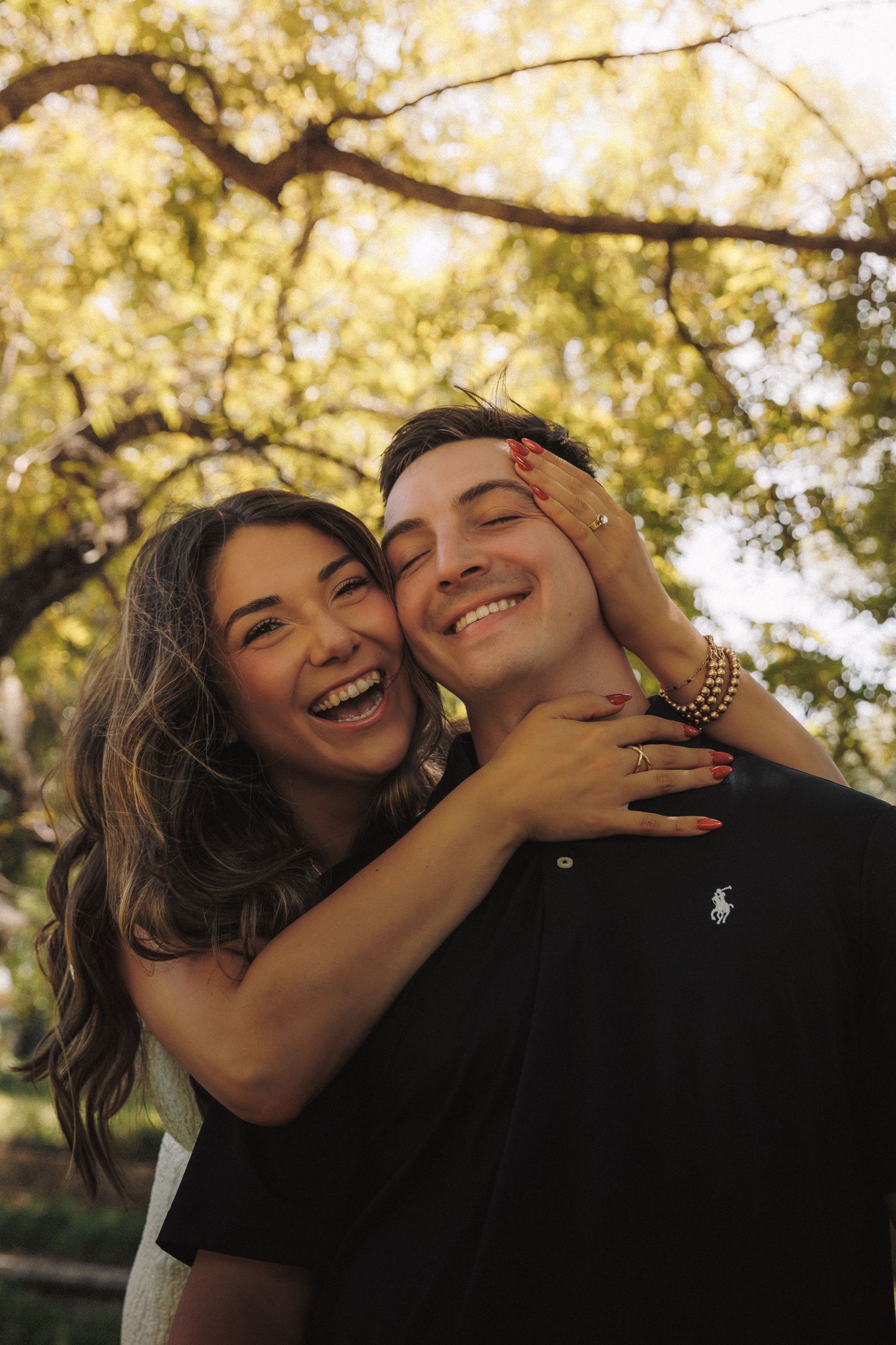 A playful couple shares joyful moments together under golden sunlit trees in a romantic outdoor photoshoot.
