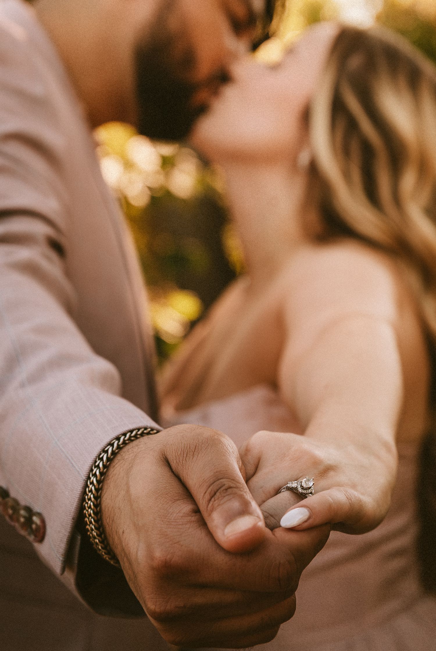 Close-up shot of hands touching while wearing an engagement ring in warm sunlight.