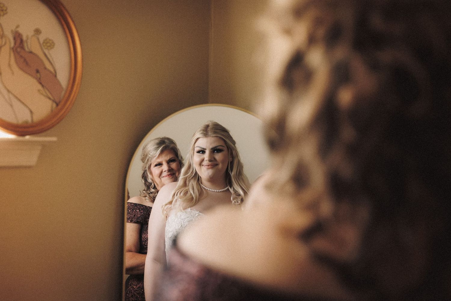 Bride and her mother share a tender moment reflected in a vintage mirror during wedding preparations.